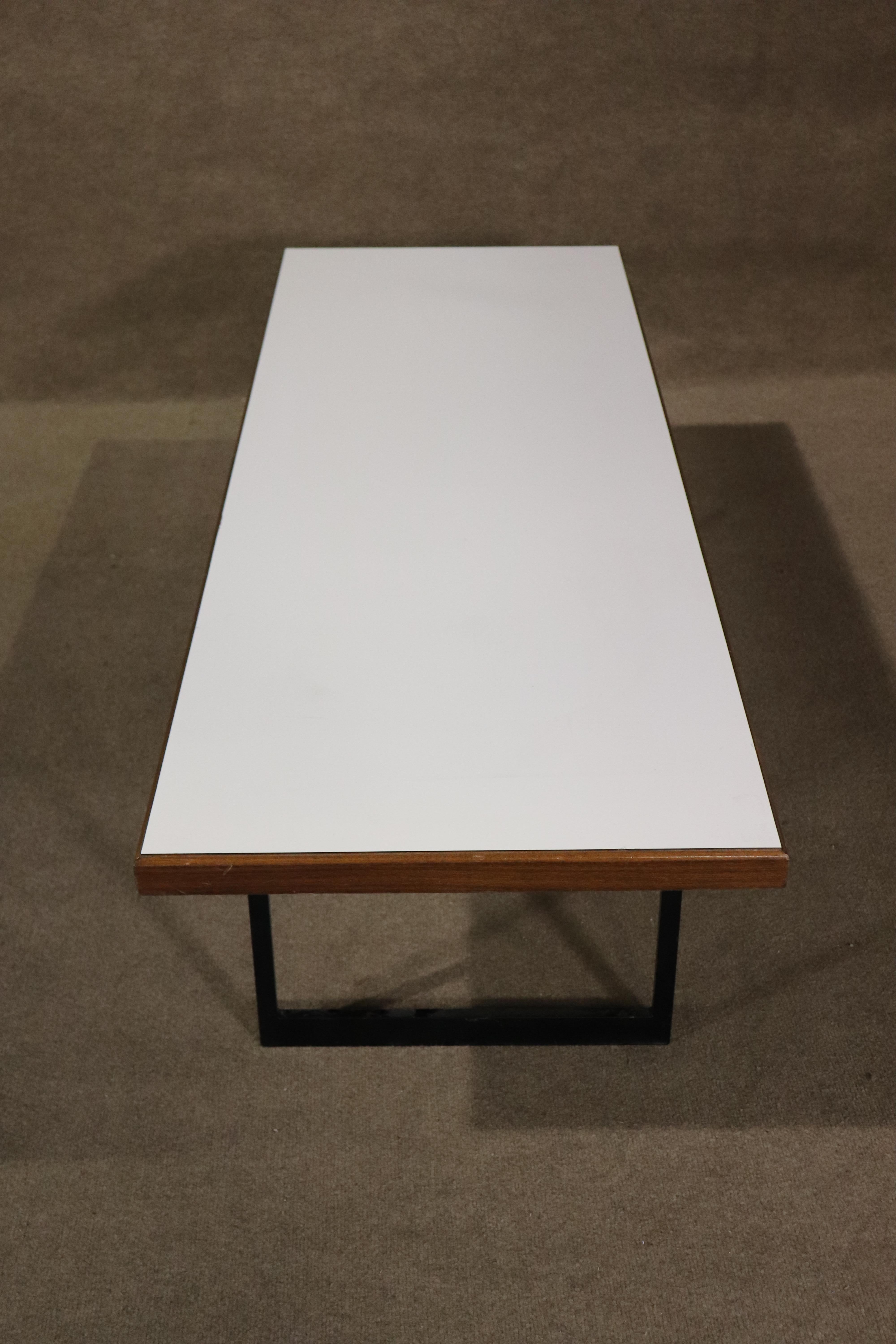 Long five foot table or bench with white laminate top over walnut wood grain. Set on a black metal base.
Please confirm location NY or NJ
