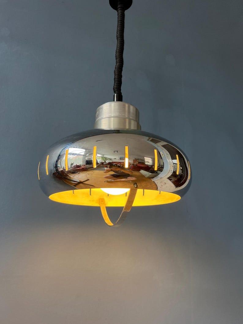 Mid century UFO pendant lamp with decorative chrome frame. The height of the lamp can easily be adjusted with the suspension mechanism. The lamp requires one E27/26 (standard) lightbulb.

Additional information:
Materials: Metal
Period: