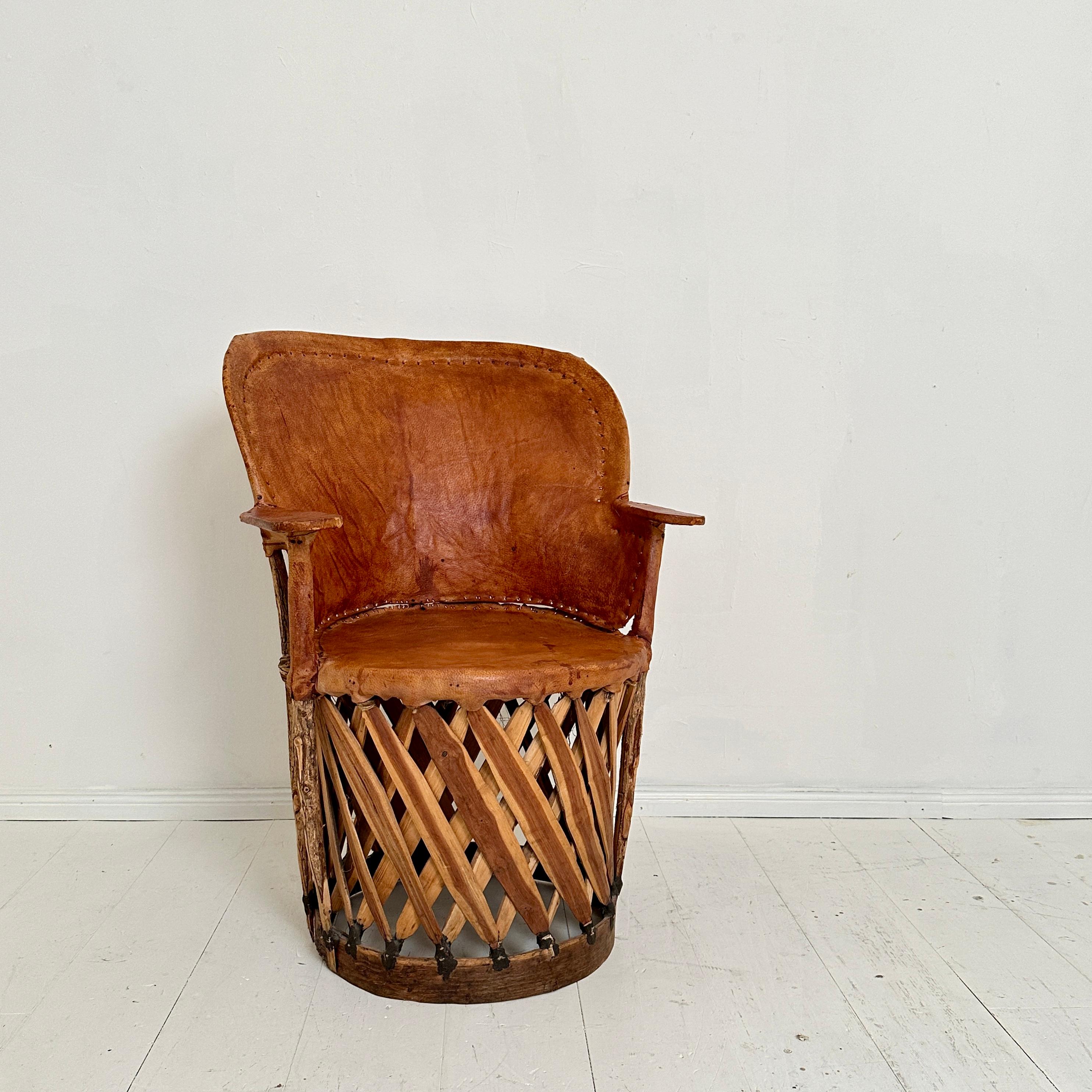 This mid-century Mexican Equipales armchair, crafted around 1970, exudes rustic charm. Its robust wooden frame provides a sturdy base, while the seating surface is formed from supple brown leather. The leather, showing signs of its age and use,