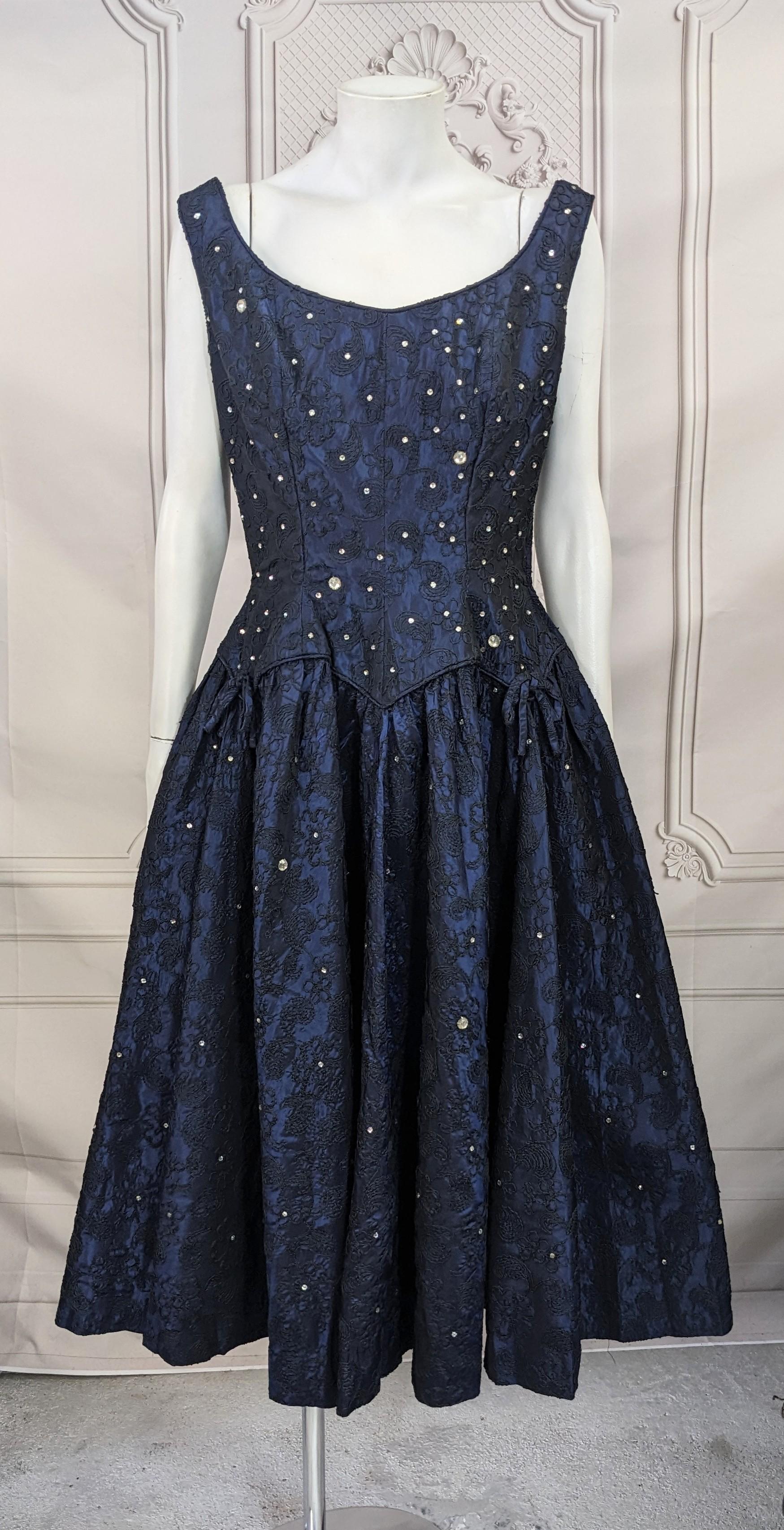 Robe de cocktail en taffetas incrustée de cristaux bleu nuit datant des années 1950. Taille cintrée avec une ligne d'épaule large et une jupe très ample. Taffetas bleu nuit avec broderie passementerie noire et cristaux sertis à la main. Taille