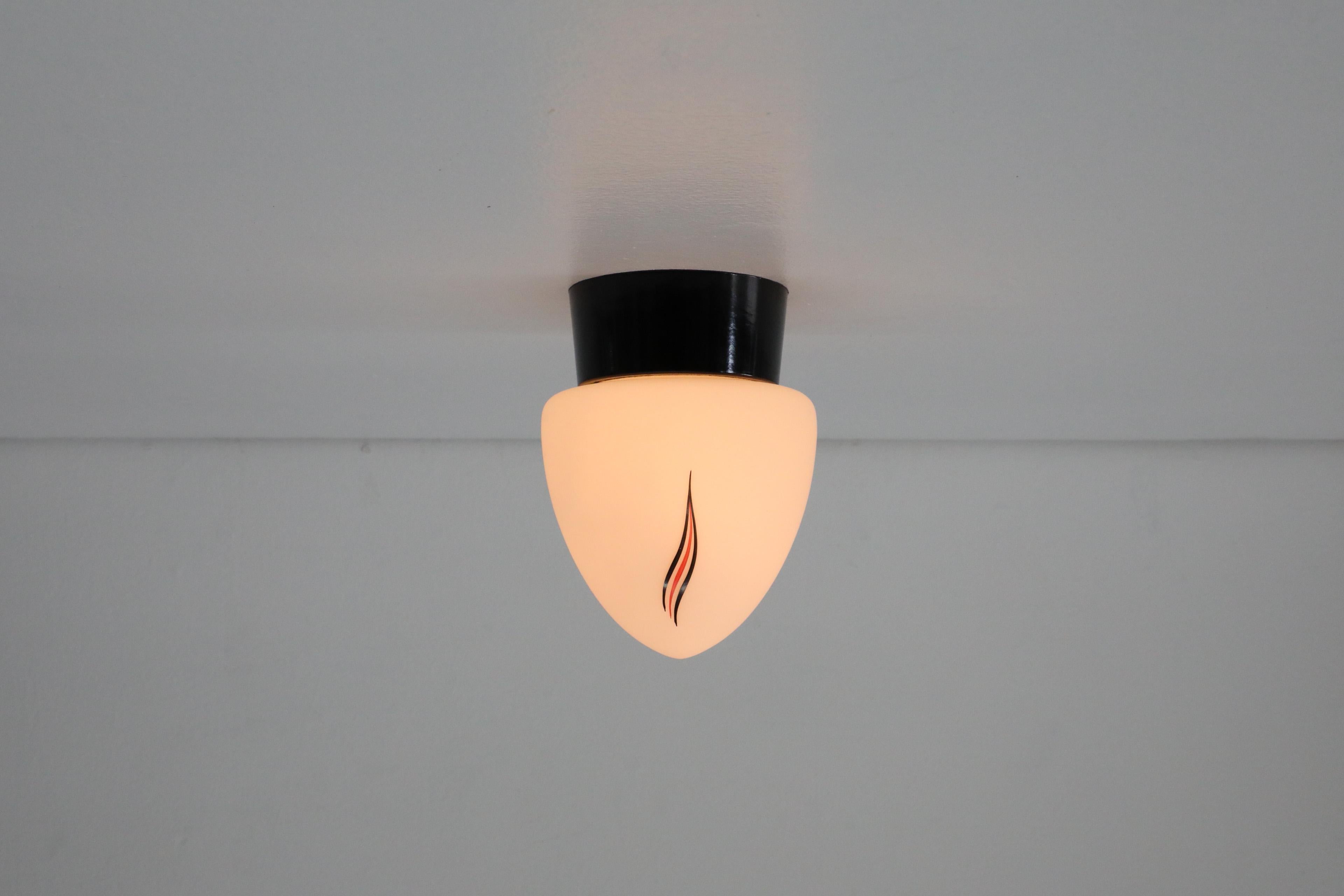 1950s printed milk glass ceiling or wall sconce with painted flame detail and black acrylic base by Thabur, a lighting and small appliance company that was founded in 1925 in the Hague, Netherlands. In original condition with age appropriate wear.