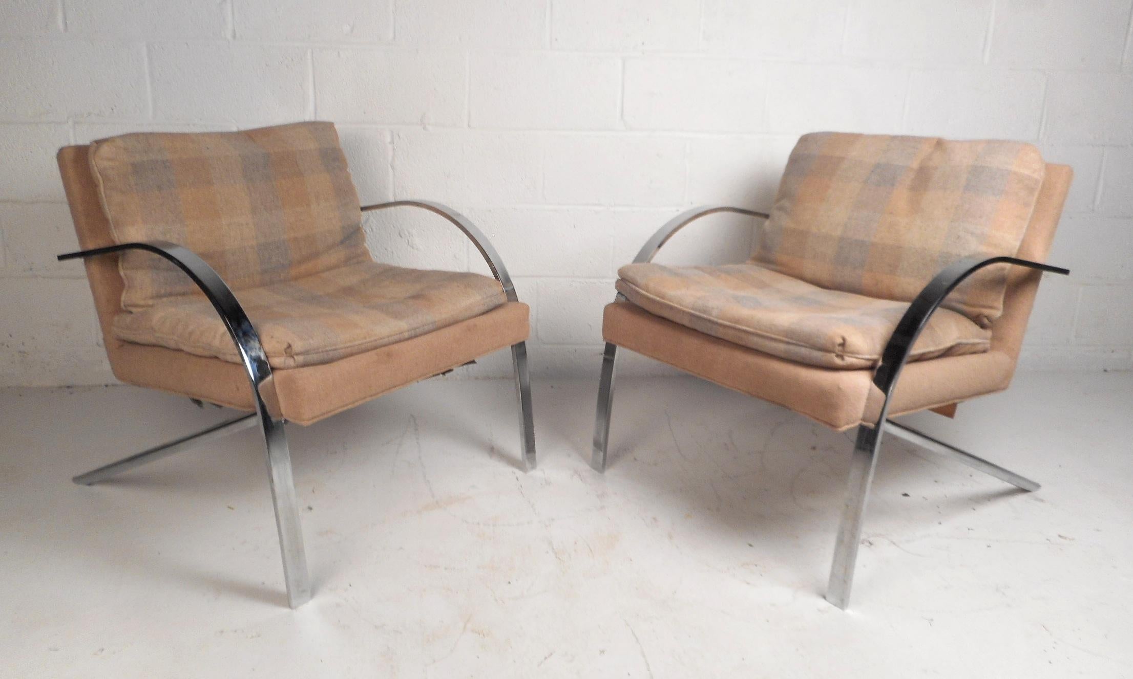 This stunning pair of vintage modern lounge chairs features heavy flat bar chrome frames and thick padded cushions. A one of a kind pair with rounded arm rests, angled back legs, and two overstuffed removable cushions. The sleek design is