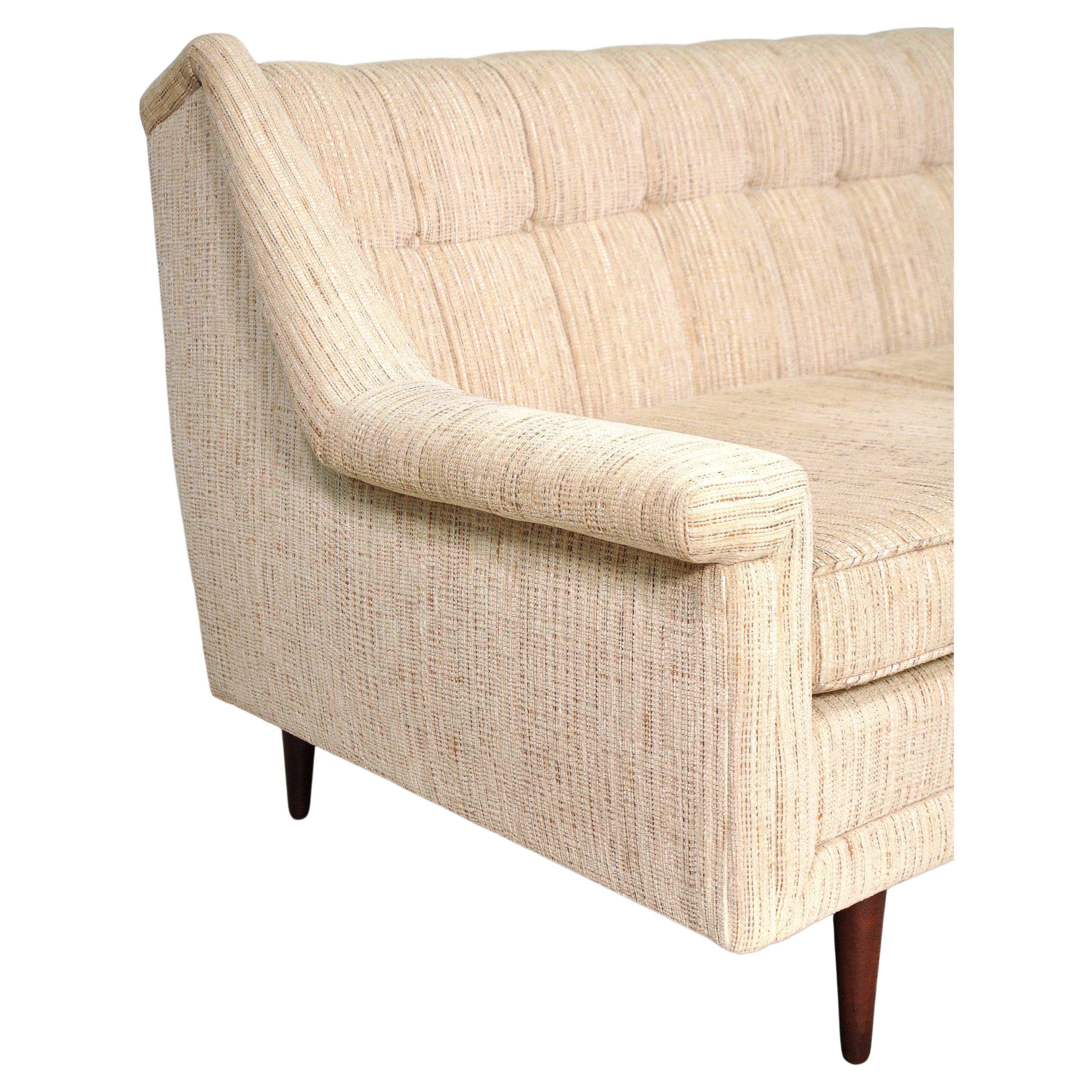 A neutral vintage Milo Baughman style cream couch with walnut legs, dating from the 1960s. The vintage three-seat sofa features the original pale beige chenille, a tufted channel back, loose cushions and round tapered legs. Very comfortable, neutral