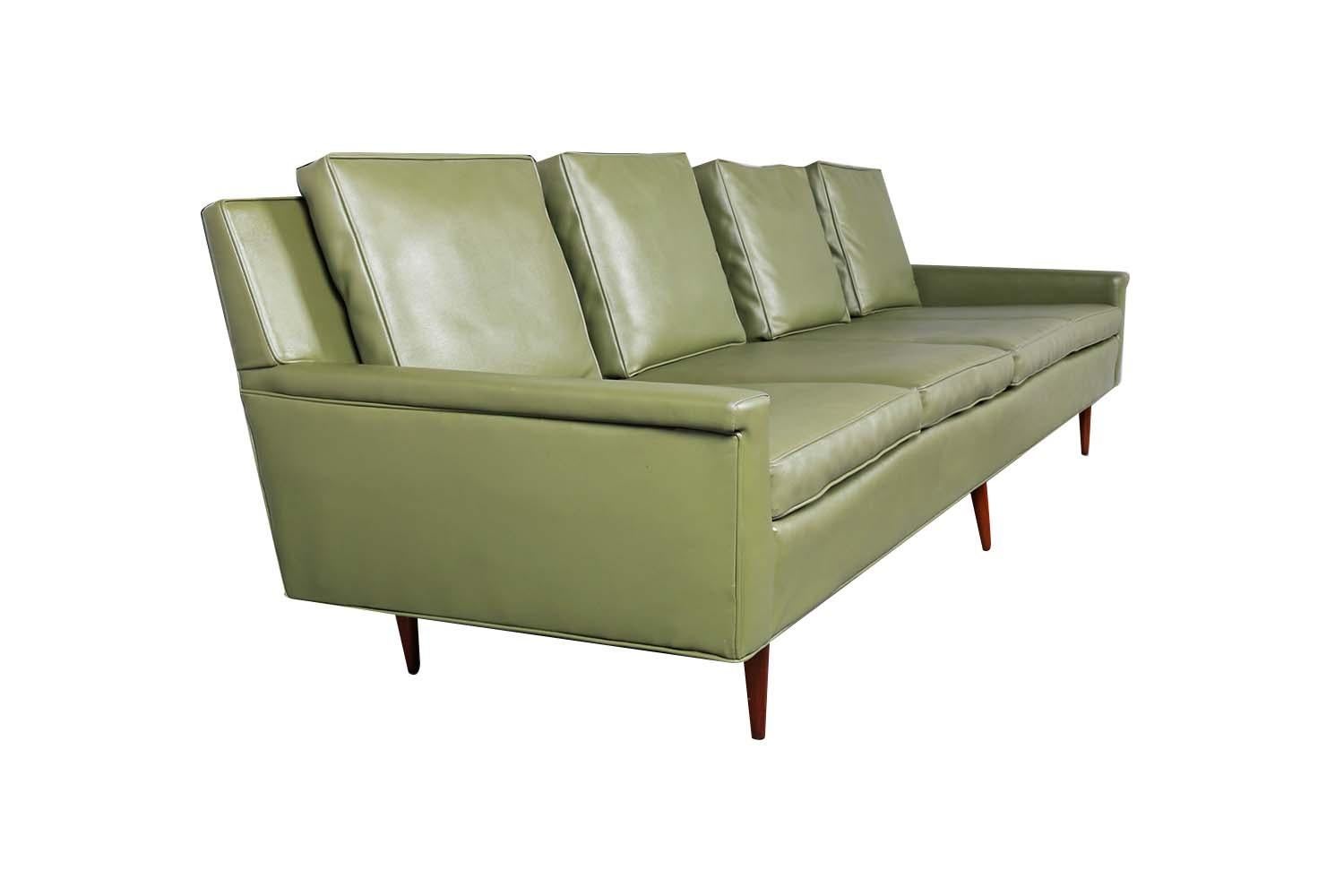 A very attractive long, four-seater upholstered sofa. Features original Naugahyde upholstery, four removable zippered seat cushions that are well intact, and four loose back cushions. The tight back and clean modern lines give this sofa a sleek