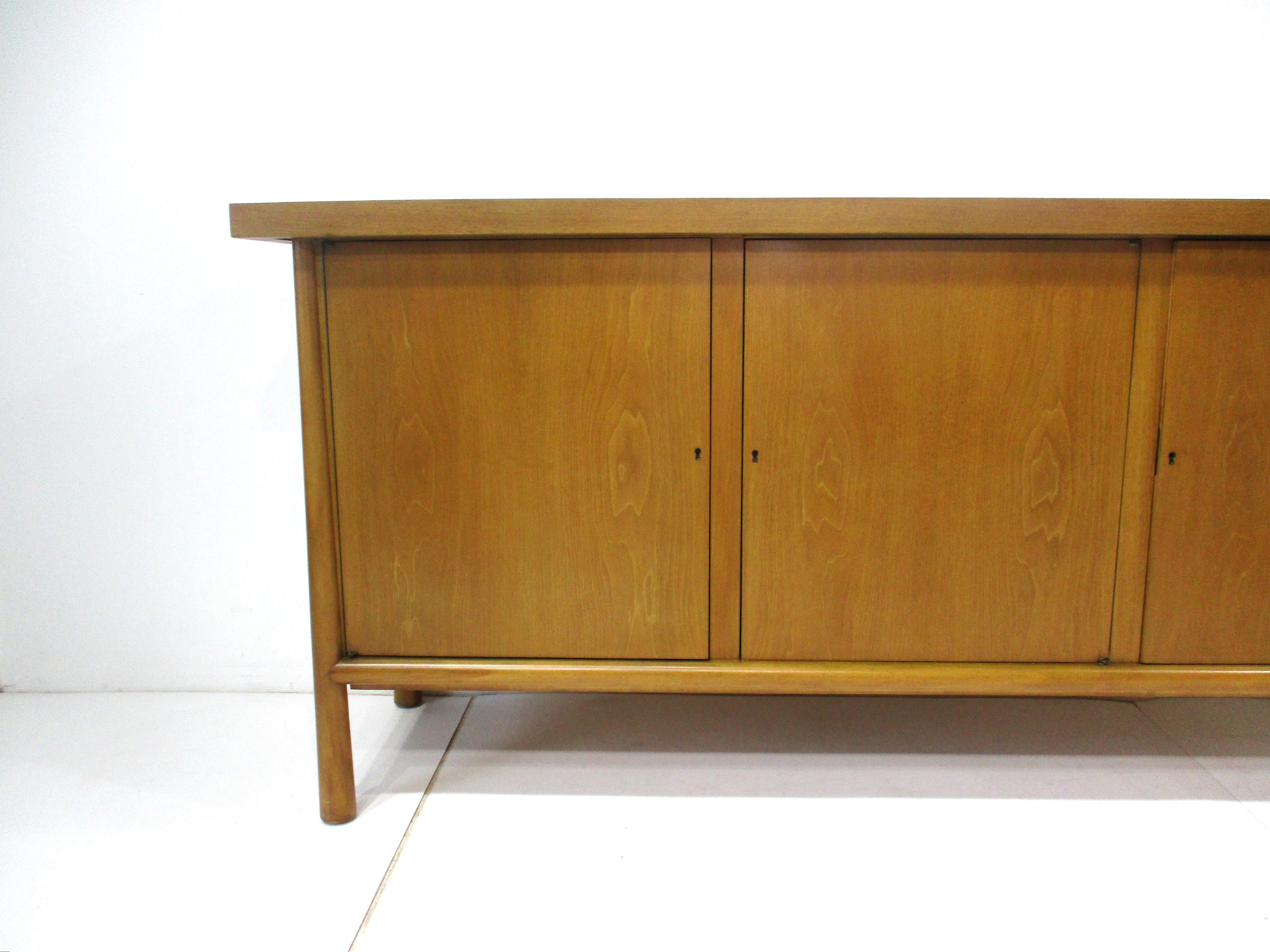 A very well crafted honey toned mahogany three door Ming sideboard or credenza , to each side door there is one adjustable shelve and to the center section four drawers , the top and bottom drawer have open storage and the center two have dividers