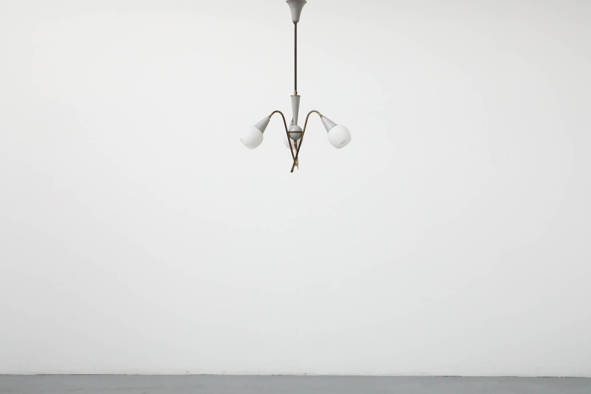 Elegante e minuscolo lampadario a tre bracci in stile Stilnovo. Questo pezzo presenta una struttura in ottone con accenti smaltati in grigio e paralumi in vetro smerigliato. In condizioni originali, con un'usura appropriata all'età, tra cui alcune