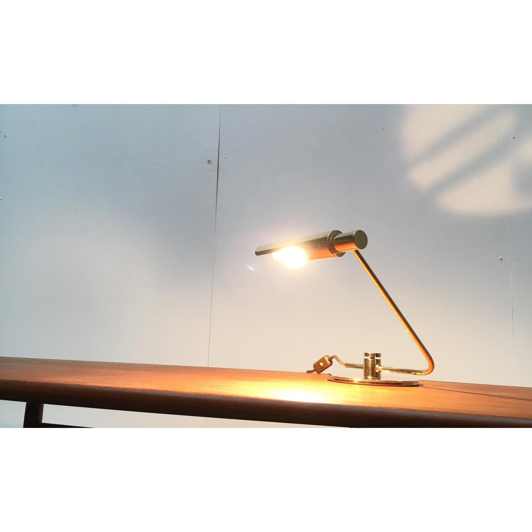 Imponente lampada da tavolo in ottone. È attribuito al produttore svizzero Baltensweiler.

Un design semplice con un'elevata variabilità. La testa della lampada cilindrica si trova all'estremità di un braccio angolato. Il tutto è fissato in una base