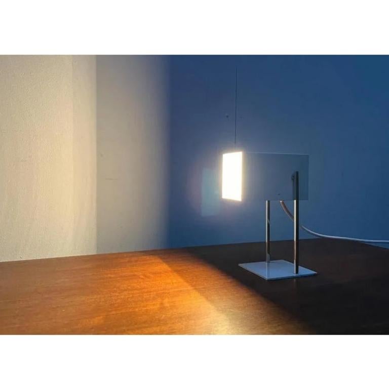 Small table lamps from Emperor shine.

A minimalist design with a cubic basic form. The simple luminaire head is open and movable on one side. It can be tilted and aligned.
The shaft consists of two parallel four -cans, which are chrome -plated. The
