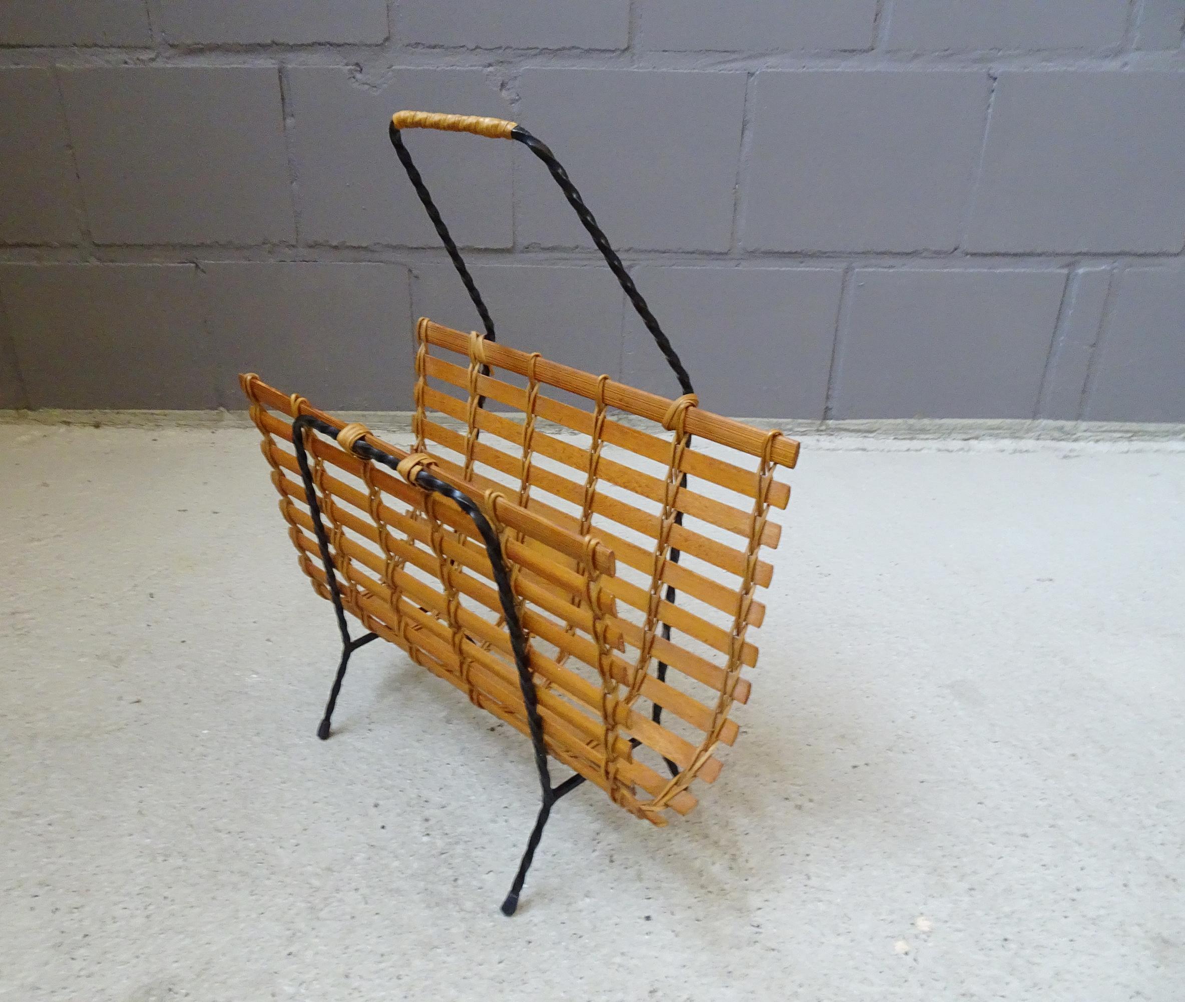 Large mid-century magazine rack made of twisted iron, narrow wooden slats, and rattan. Minimalist 1960s design made from natural materials. The raised handle, which gives it a unique look, is particularly characteristic.

A timeless classic for