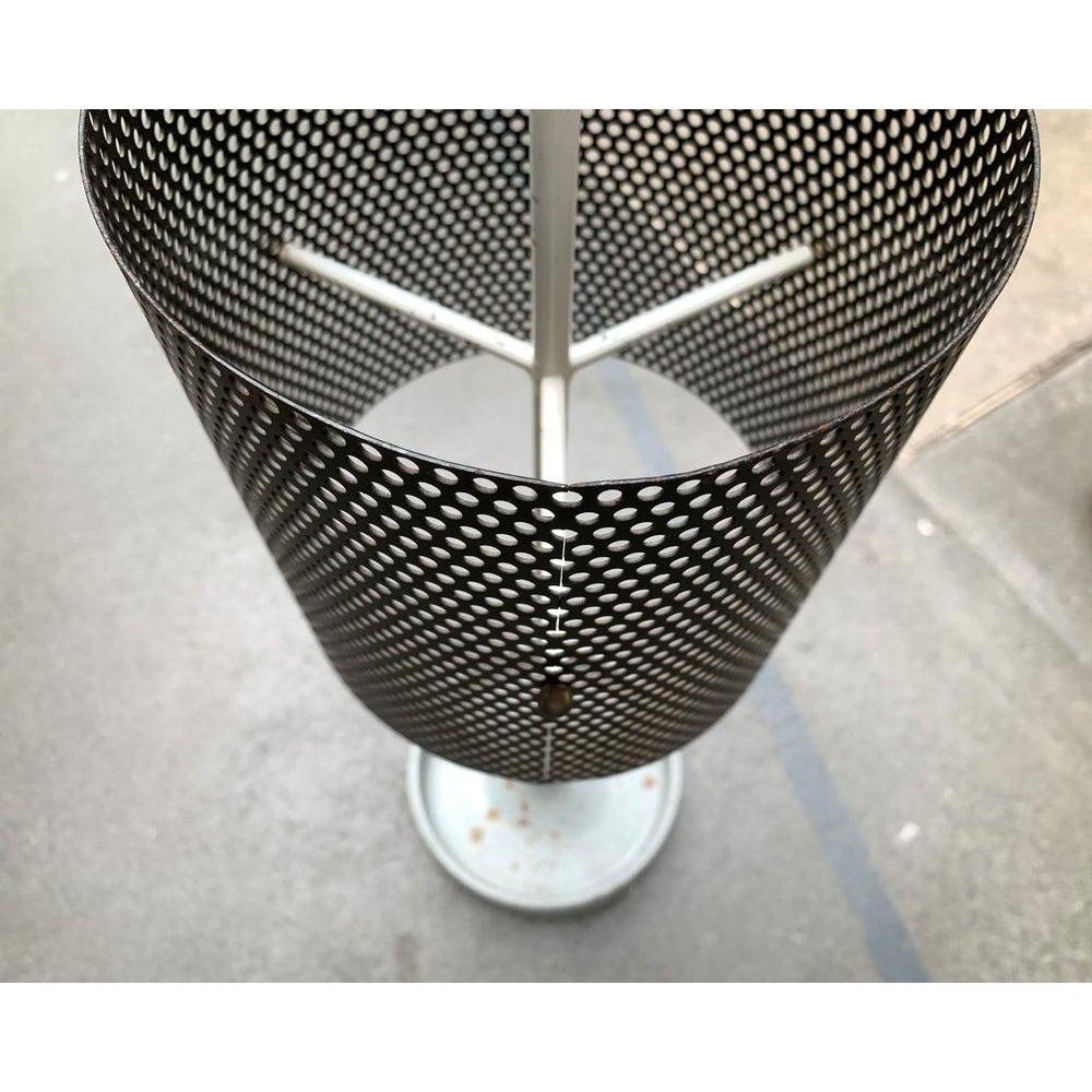 Der perforierte Ring zur Aufnahme der Schirme schwebt als transparenter Körper in Höhe des oberen Drittels des Schafts. Eine schwere gusseiserne Wanne dient als Fuß.

Zusätzliche Informationen:
MATERIALIEN: Metall
Farbe: Schwarz
Stile: Moderne Mitte