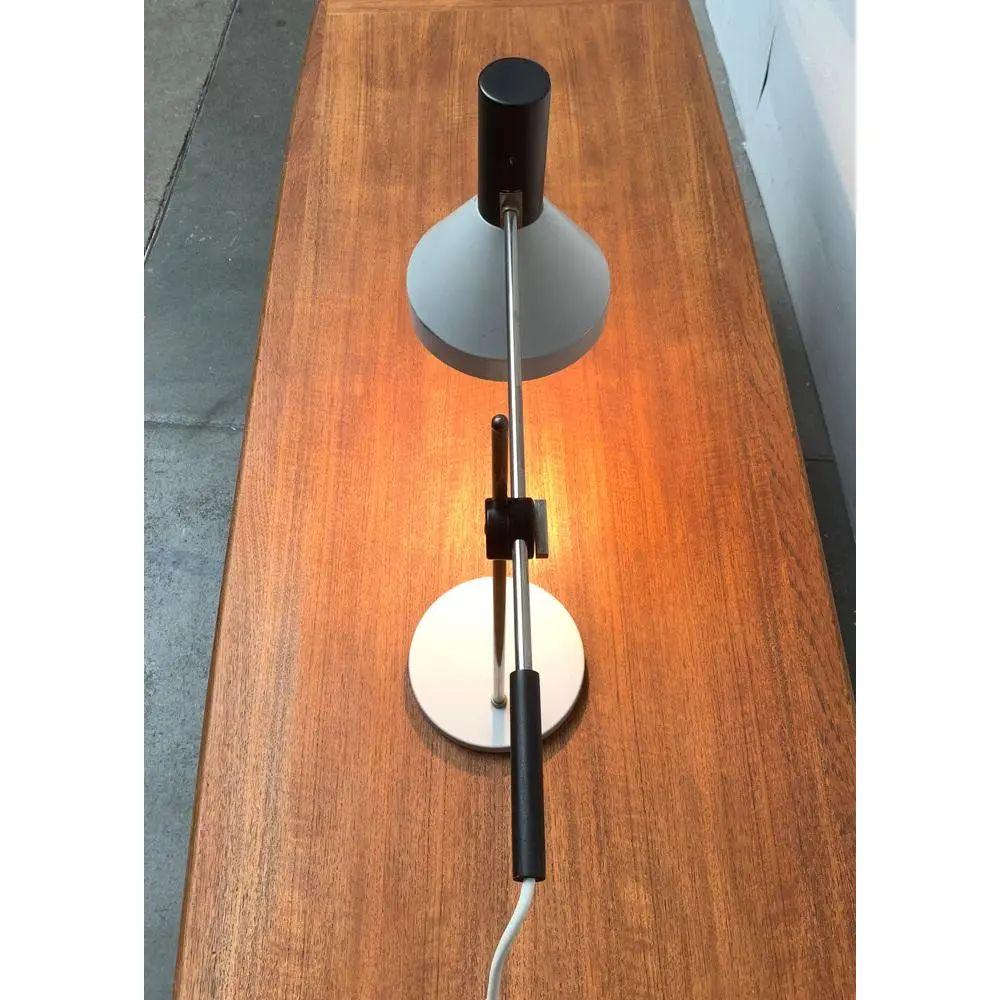 Minimalist Mid-Century table lamp.

Simple table lamp in gray and black. The umbrella shows a classic funnel shape. The foot is a simple plate foot on which the shaft is asymmetrically mounted. The arm can be adjusted and tilted over a joint on the