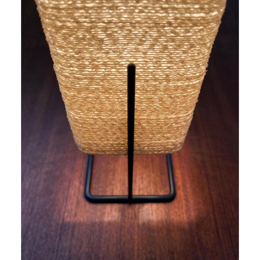 Lámpara de mesa minimalista con una base llamativa.

La pantalla está hecha de algún tipo de plástico o fibra de vidrio. En el exterior muestra una estructura tosca. El detalle más llamativo es la base minimalista. Una horquilla finamente diseñada