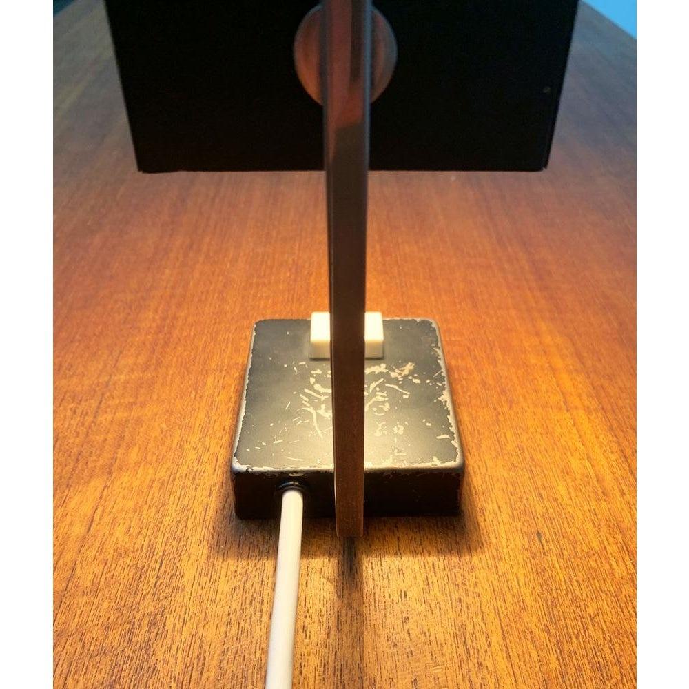 Small Mid Century table lamp.

A minimalist design with clear lines. Foot and screen are cuboid and connected to a shaft. The screen can rotate about its axis and the light is aligned. The top of the screen shows centrally a fine perforation that