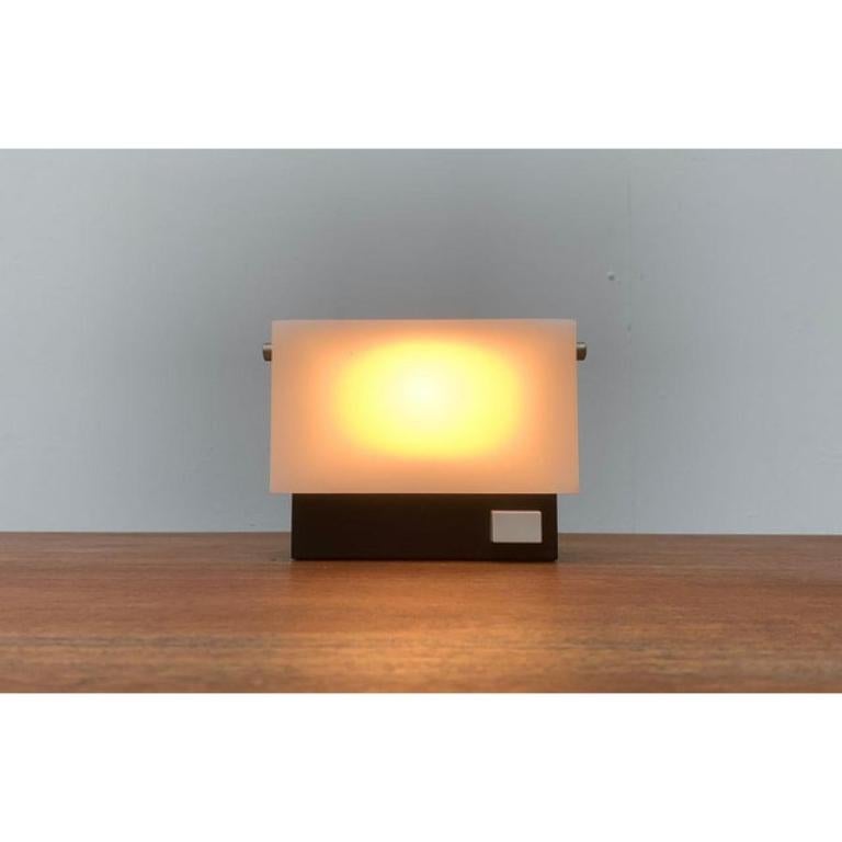 Rare Mid Century table lamp.

A minimalist design. The lamp body is a simple box made of metal. A diffuser made of translucent plastic at the front can be folded upwards, which gives the lamp a changing appearance and changes the light effect.
A