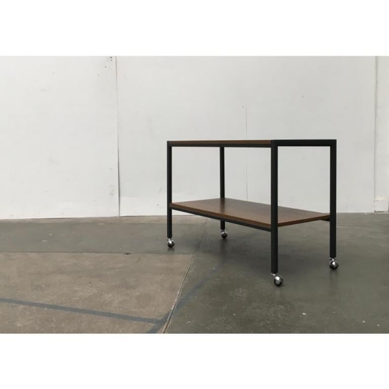 Chariot ou table d'appoint roulante en teck du milieu du siècle dernier. Chariot simple avec plateaux en teck et structure en métal foncé. Le cadre est en tube carré et s'harmonise en forme et en couleur avec les plateaux plaqués en teck. Les