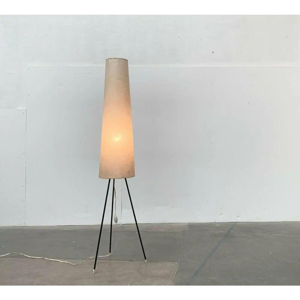 Minimalistische Mid Century Tripod Stehleuchte.

Schlichte Stehlampe mit fein gestaltetem dreibeinigem Fuß. Der Farbton läuft leicht konisch nach oben. Die Lampe ist in sehr gutem Zustand mit Gebrauchsspuren und Reparaturen am Schirm. Europäischer