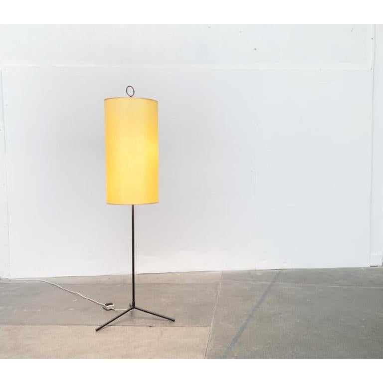 Semplice lampada da terra del Mid Century con un sorprendente piede a treppiede.

Un design minimalista. Lo schermo ha una semplice forma cilindrica ed è ricoperto da un materiale tessile. Colpisce il Tripodfuß nero con l'asta sottile, che scompare
