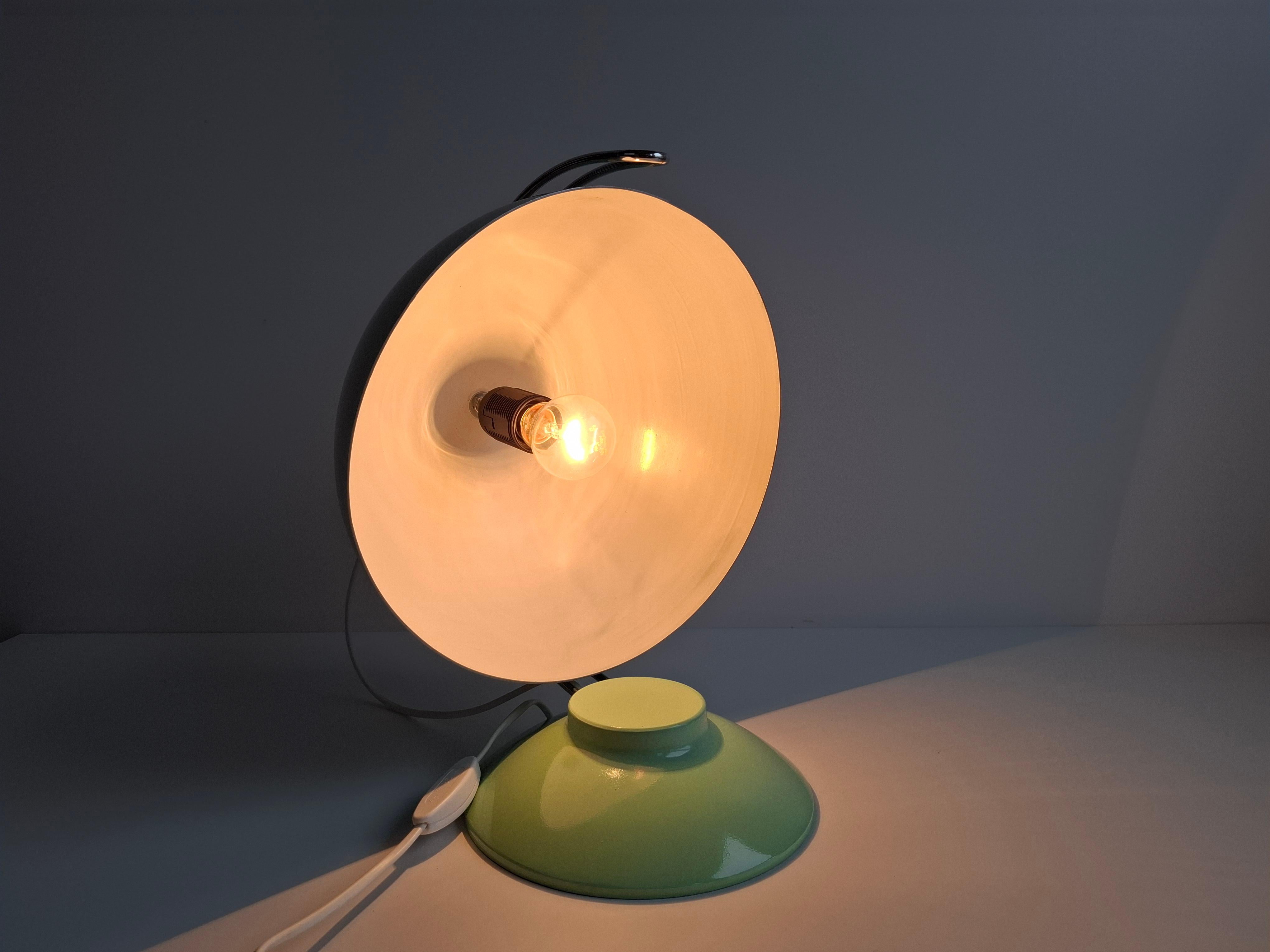 This 1970s Czechoslovak mid-century desk lamp features a mint green metal dome shade supported by elegant chrome arcs. The adjustable shade allows directional lighting, making it both practical and sculptural. The lamp shows age-related
