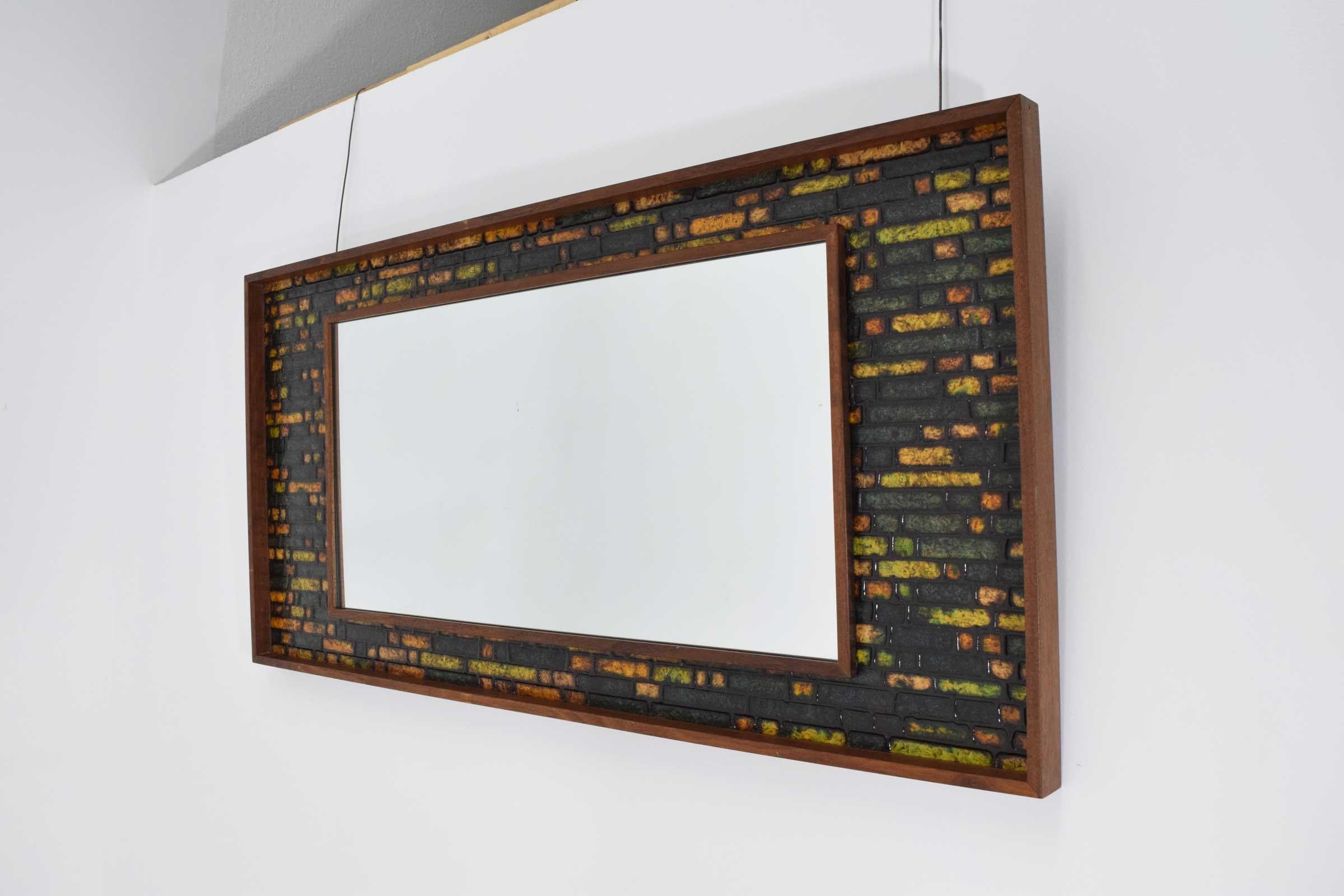 A nice mirror with tile like detail in greens, yellows, black and oranges. Walnut or teak frame. Can hang vertical or horizontal.