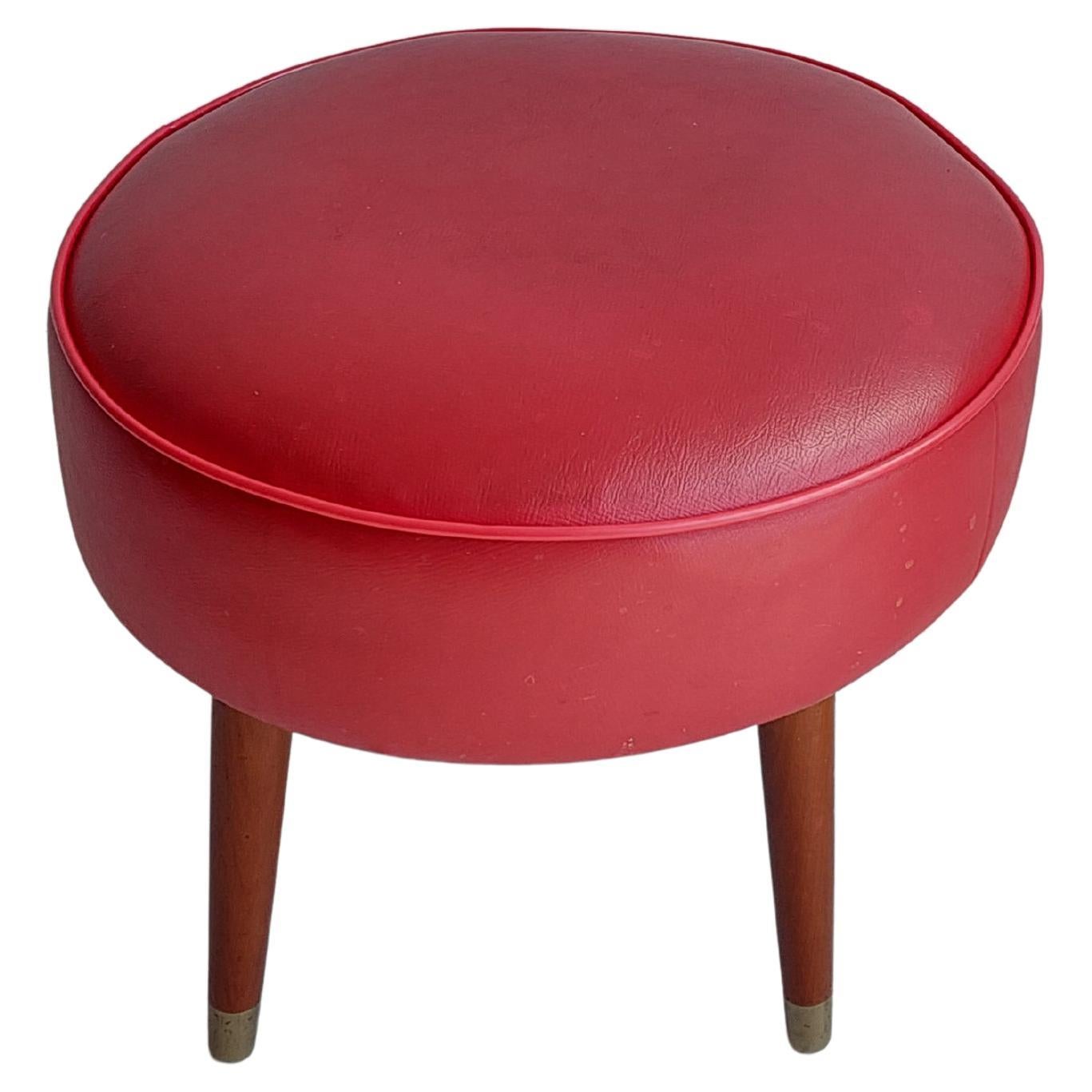 Miss Muffet foot stool in original red vinyl, on wooden legs.
Vintage Footstool, 1950's Original Upholstery, Mid-Century Modern stool.
This is an original vintage (mid 20th century) round foot stool with medium/dark red vinyl upholstery on top and