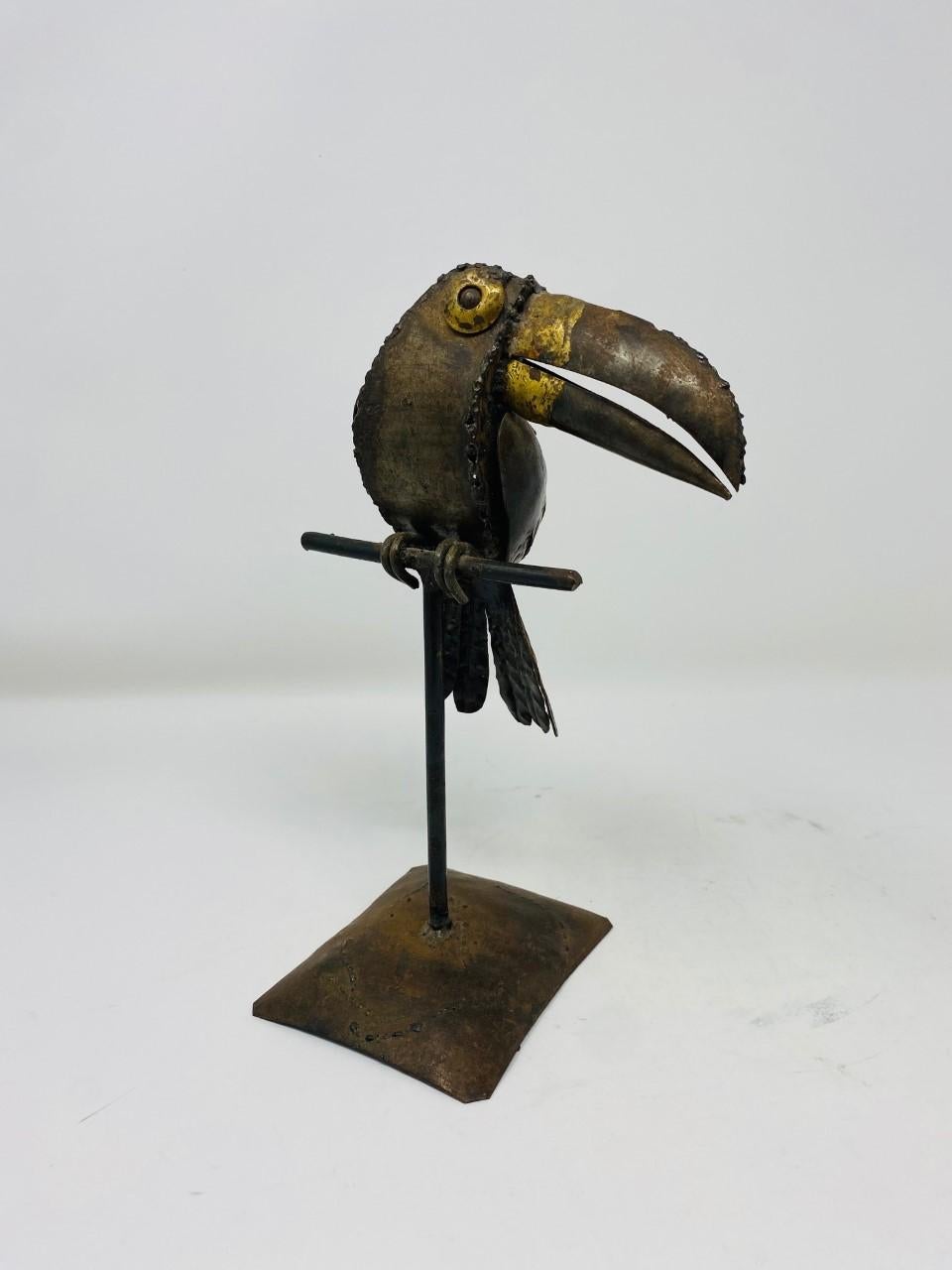 Sculptural Toucan bird on metal perch, made of mixed metals (copper, brass). This 1970s piece follows the style of Sergio Bustamante. The mix of metals adds vibrancy and depth to the form and the details on the feathering and expressions allude to
