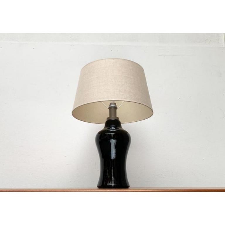 Rare table lamp of the well -known luminous designer ingo maurer from the late 1960s.

a classic design of impressive size. The ornamental curves of the large luminaire foot made of black glass are striking. The umbrella is round and covered with a