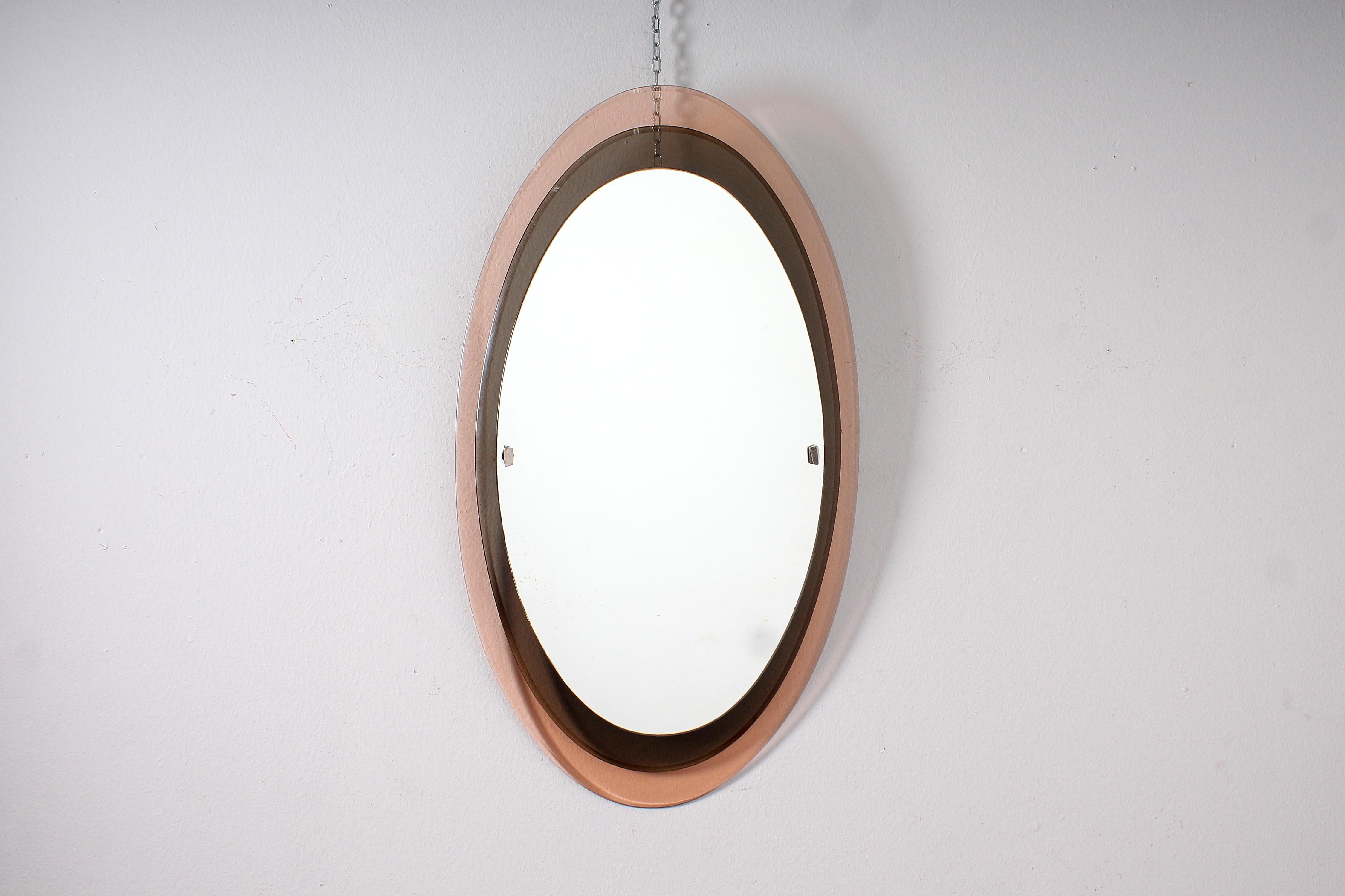 Raffinierter Spiegel mit ovalem Rahmen auf zwei Ebenen aus rosafarbenem und rauchfarbenem Glas, mit abgeschrägtem Rand und ebenfalls ovalem Spiegel. Mod. 