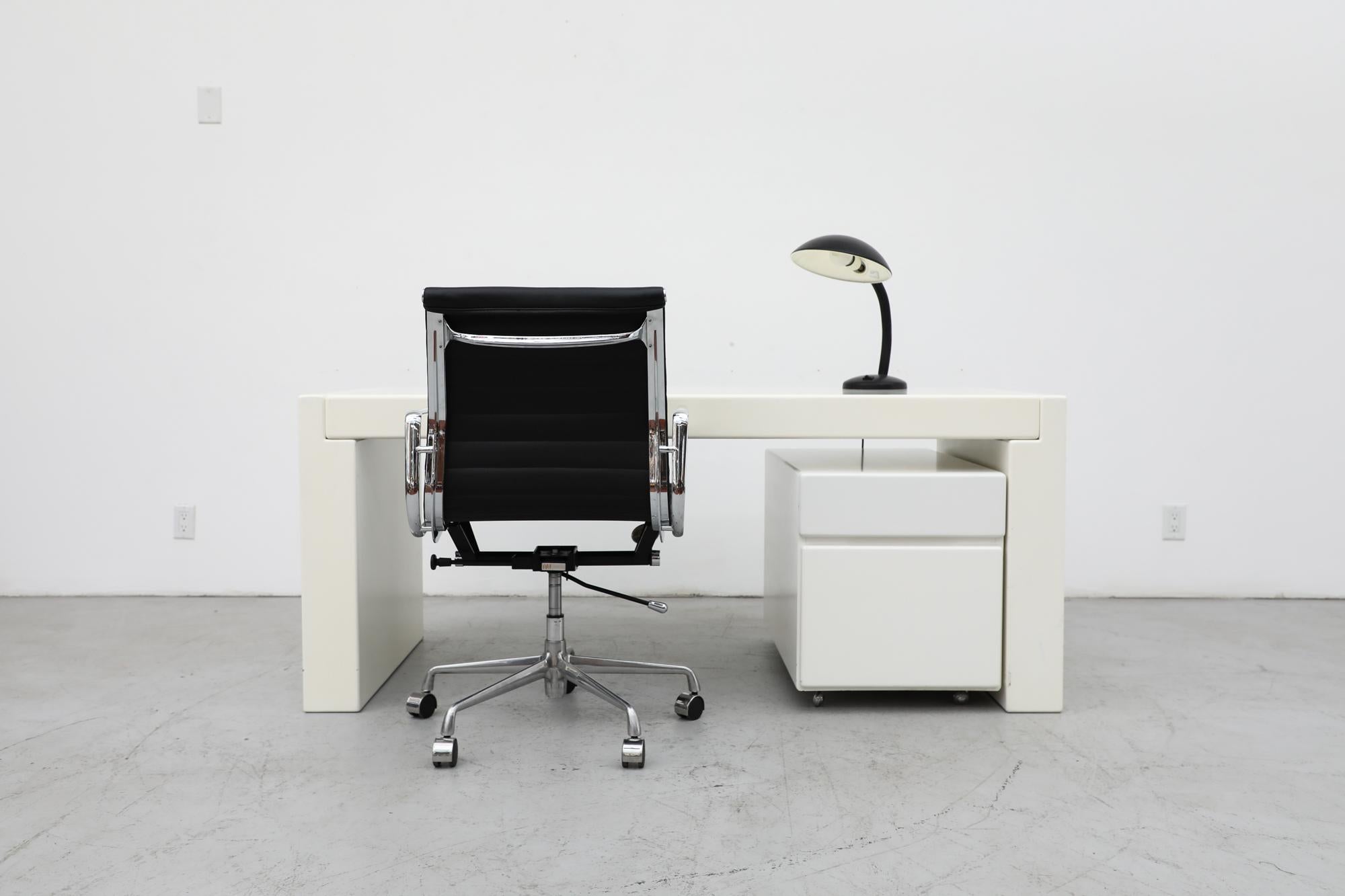 MOD Jean Maneval inspired white laminate desk with a two drawer rolling storage cabinet. In original condition with visible wear, discoloration and slight color variation between the table and the file cabinet. Visible scratching to the top and