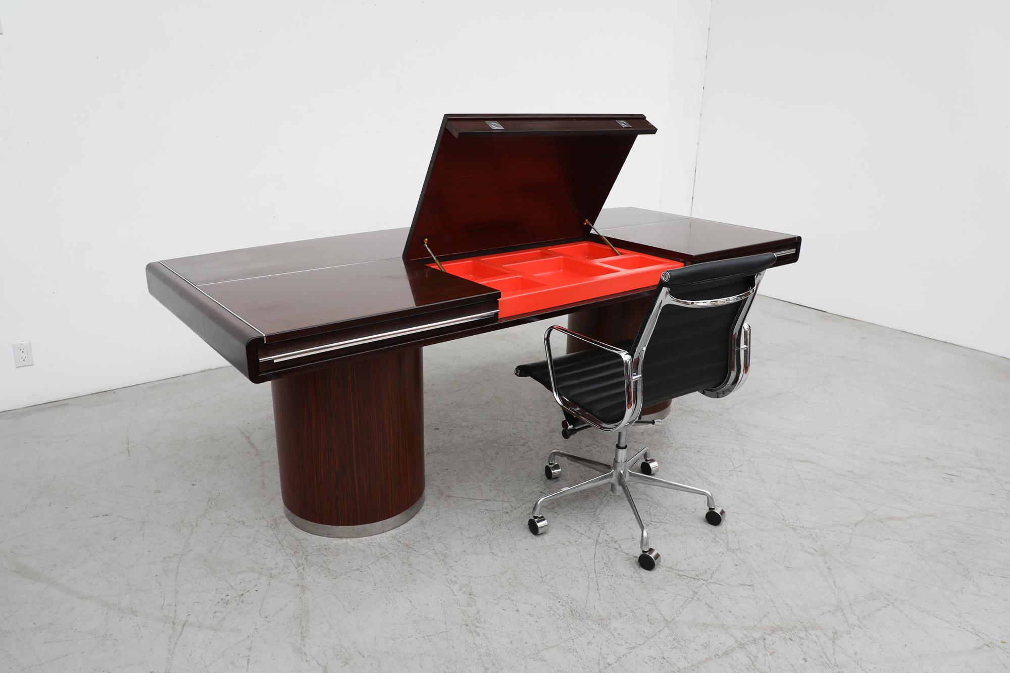 Italian midcentury MOD executive desk with a slightly bowed front, vibrant red molded plastic lined drawers and a matching desk compartment that is housed under the top that lifts up to reveal a large storage area. The top sits on 2 pillar bases