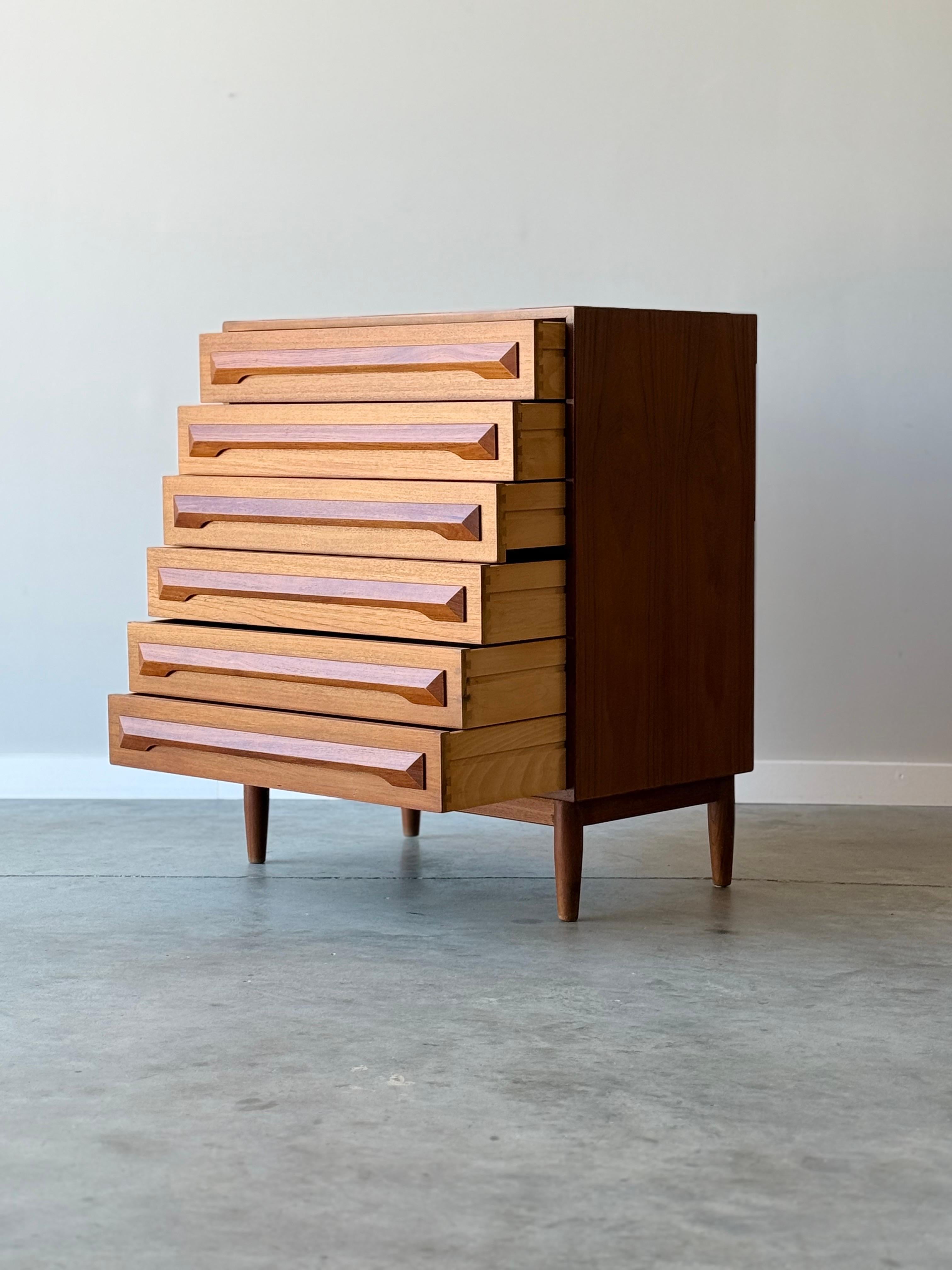 Modello di metà secolo No. 87, comò highboy in teak. Progettato da Kofod Larsen per Silkeborg Møbelfabrik, Danimarca. Dispone di sei cassetti lunghi e scorrevoli. Le maniglie rettangolari in teak intagliato accentuano ogni cassetto aggiungendo