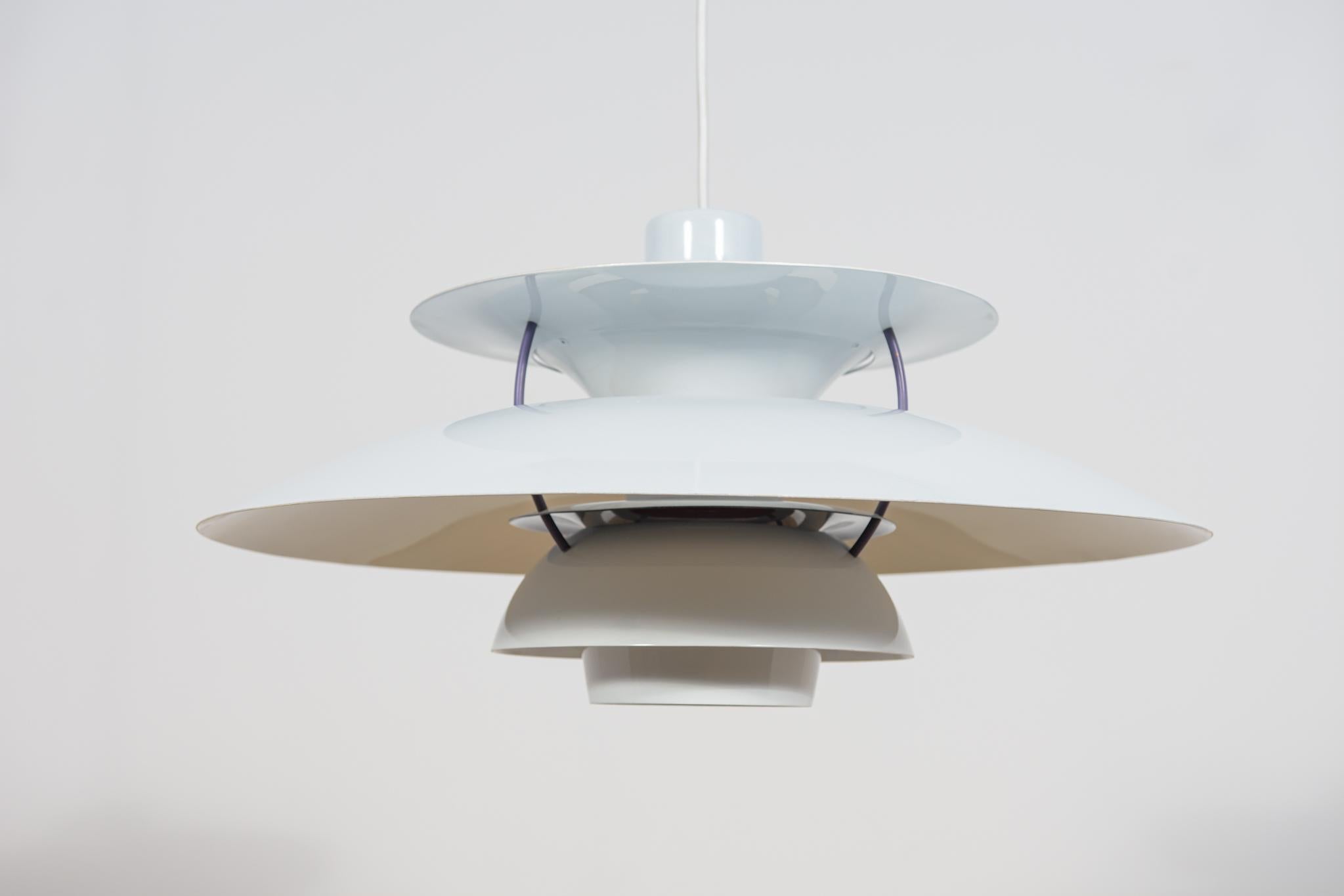 Se trata de un diseño de Poul Henningsen de 1958 basado en el principio de un sistema de tres pantallas reflectantes, que dirige la mayor parte de la luz hacia abajo. La lámpara PH5 se lanzó en 1958: el 5 de su nombre hace referencia a sus 50 cm de