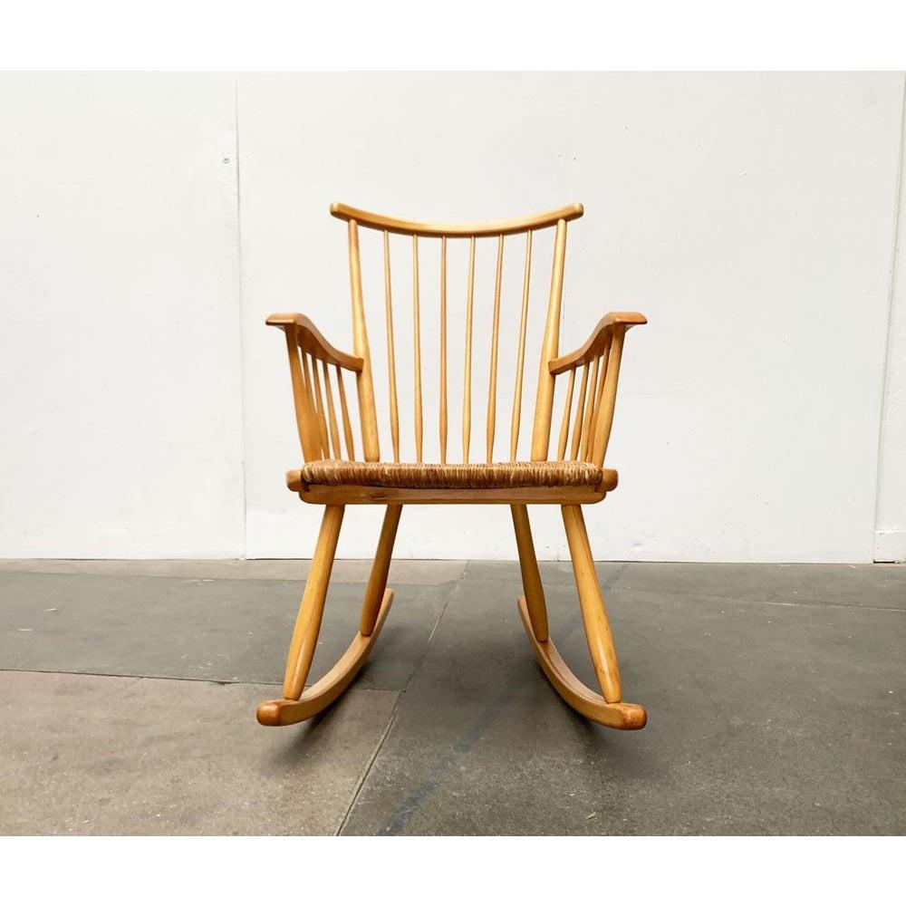 Sedia a dondolo del Mid Century di WK Möbel su disegno di Arno Lambrecht degli anni '50.

Il telaio è composto interamente da elementi in legno pieno con connessioni in parte complesse. Lo schienale e i braccioli sono di forma concava e risolti in