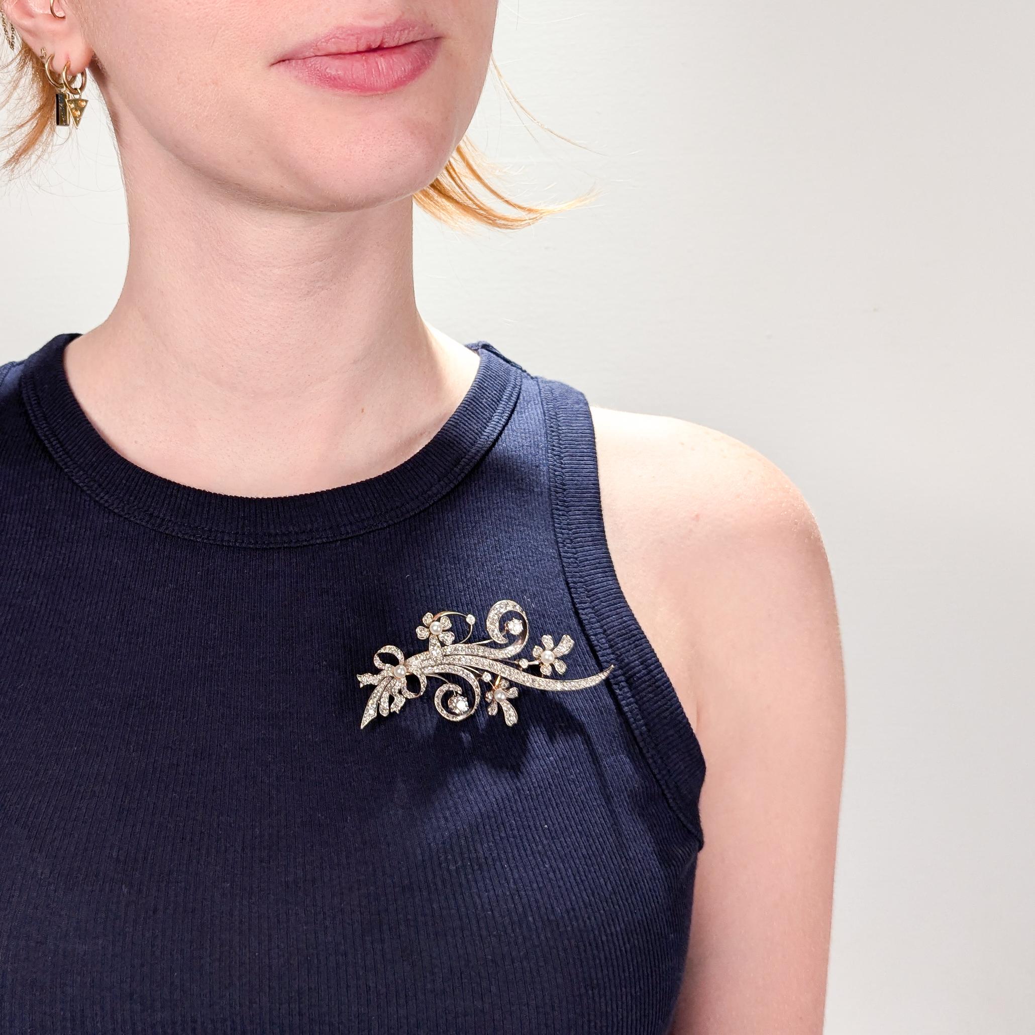 A fine Mid-Century gold, diamond, and pearl brooch.

In 14 karat white & yellow gold.

In the form of a sprig of flowers bound with a ribbon knotted at its base.

Set with 4 round cultural pearls as the pistils of the flowers and at the center of