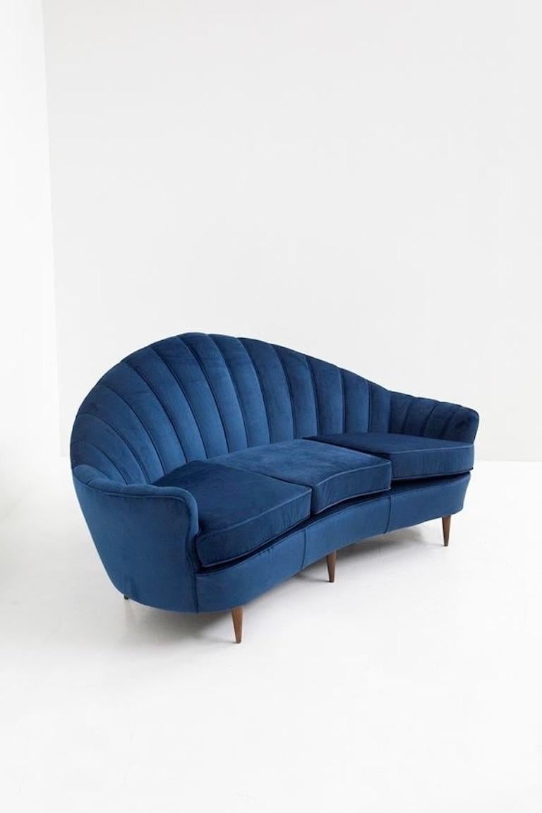 Modernes italienisches Sofa aus der Jahrhundertmitte der 1950er Jahre, das Guglielmo Ulrich zugeschrieben wird. Muschelförmig in blauem Samt. mit Holzfüßen.
Dieses Sofa besticht durch seine elegante Form und die vielen Details in seinem
