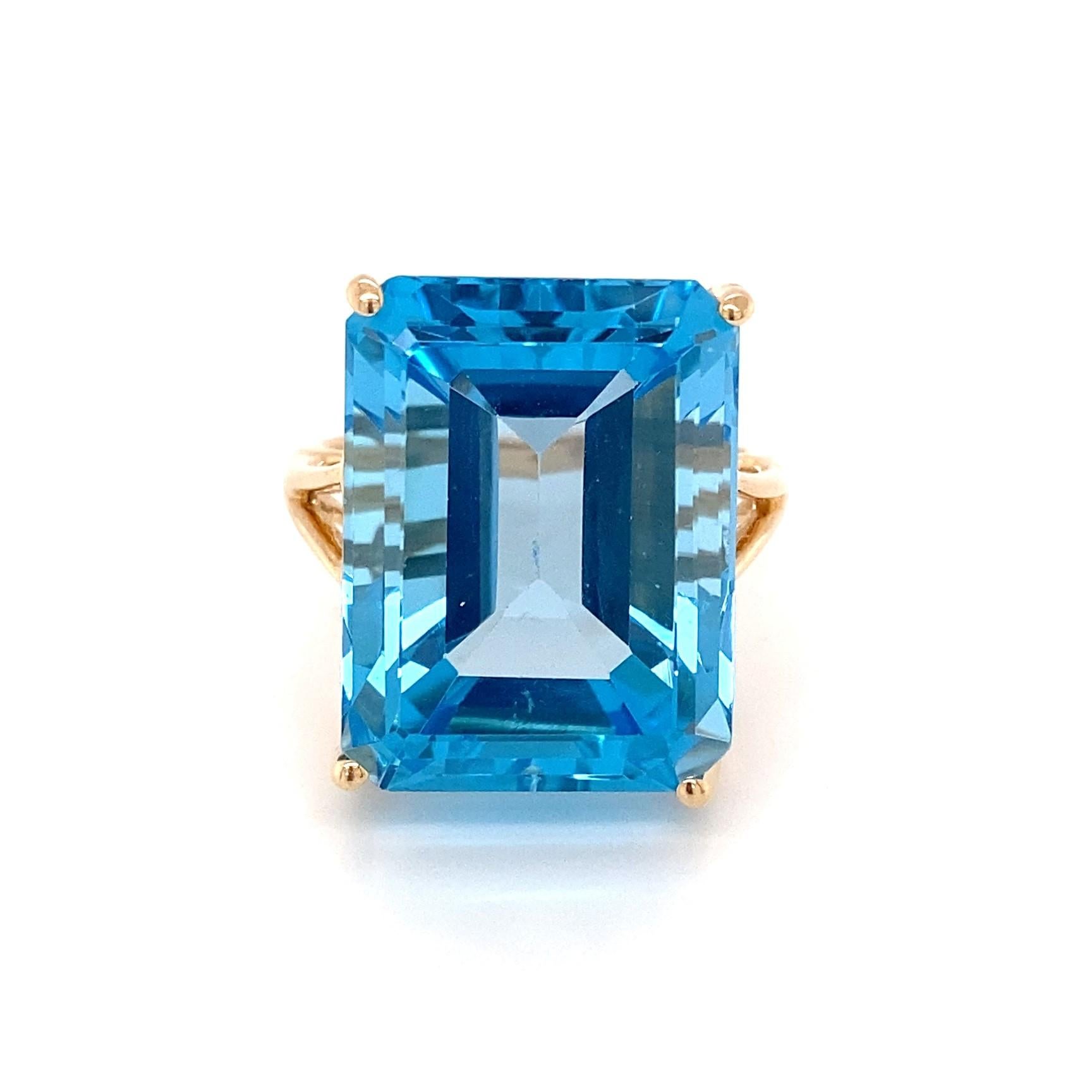 This mid-century modern 14 karat yellow gold ring holds an exquisite blue topaz that beckons you to take a dive into its intense blue swimming pool. The high quality emerald-cut blue topaz is elegantly proportioned in its high profile and measures
