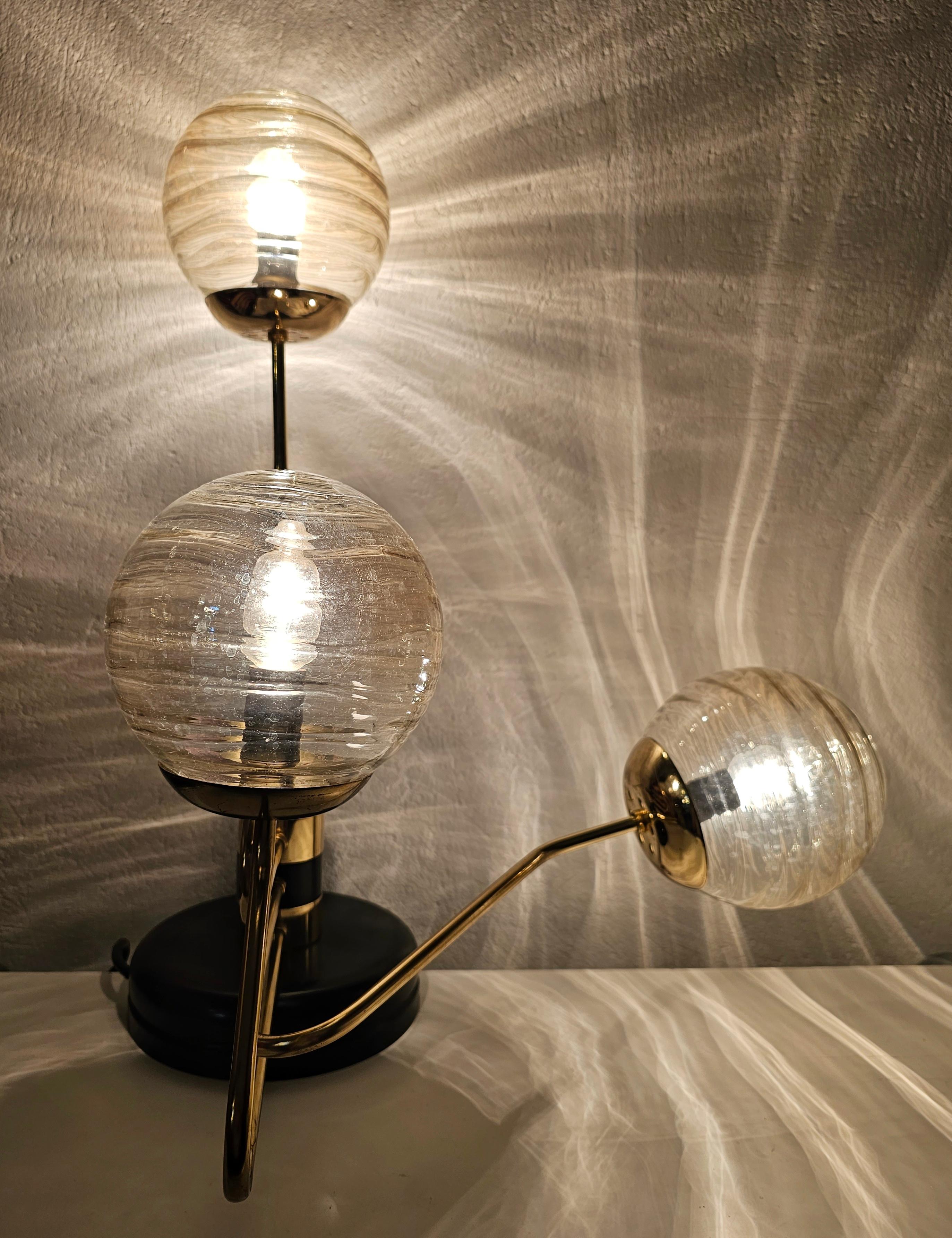 In diesem Angebot finden Sie eine schöne und elegante 3-armige Mid Century Modern Tischlampe im Stil von Goffredo Reggiani. Sie hat einen Sockel aus schwarzem Metall und Messing mit drei Reliefgläsern/Kugeln mit goldfarbenem Ton. Zwei der drei Arme