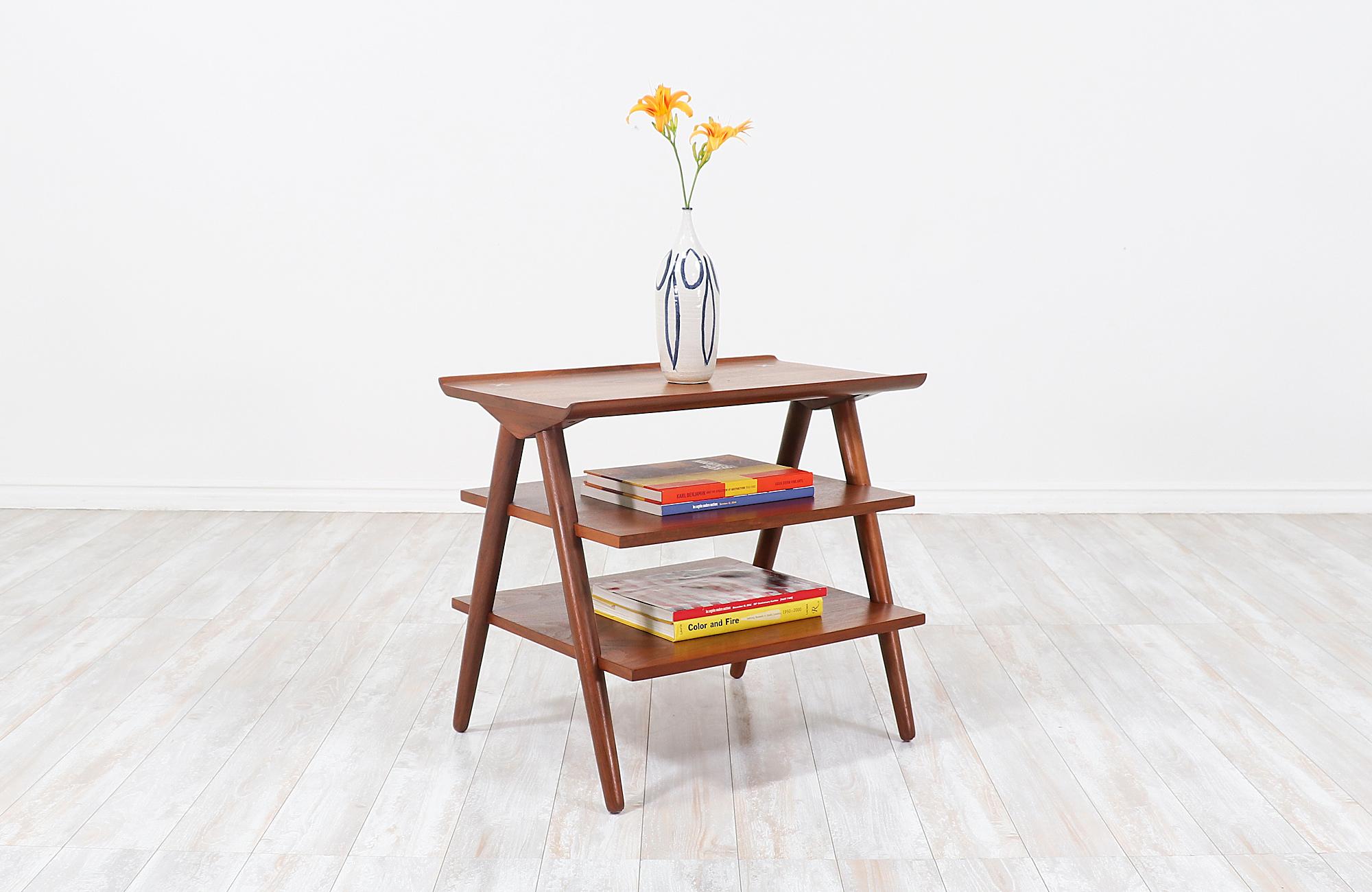 Mid-Century Modern side table designed by Merton Gershun and manufactured by American of Martinsville in the 1960s. Constructed from solid walnut, this sculpted side table features a flight of 3-tier shelves and a raised edge on the top tier while