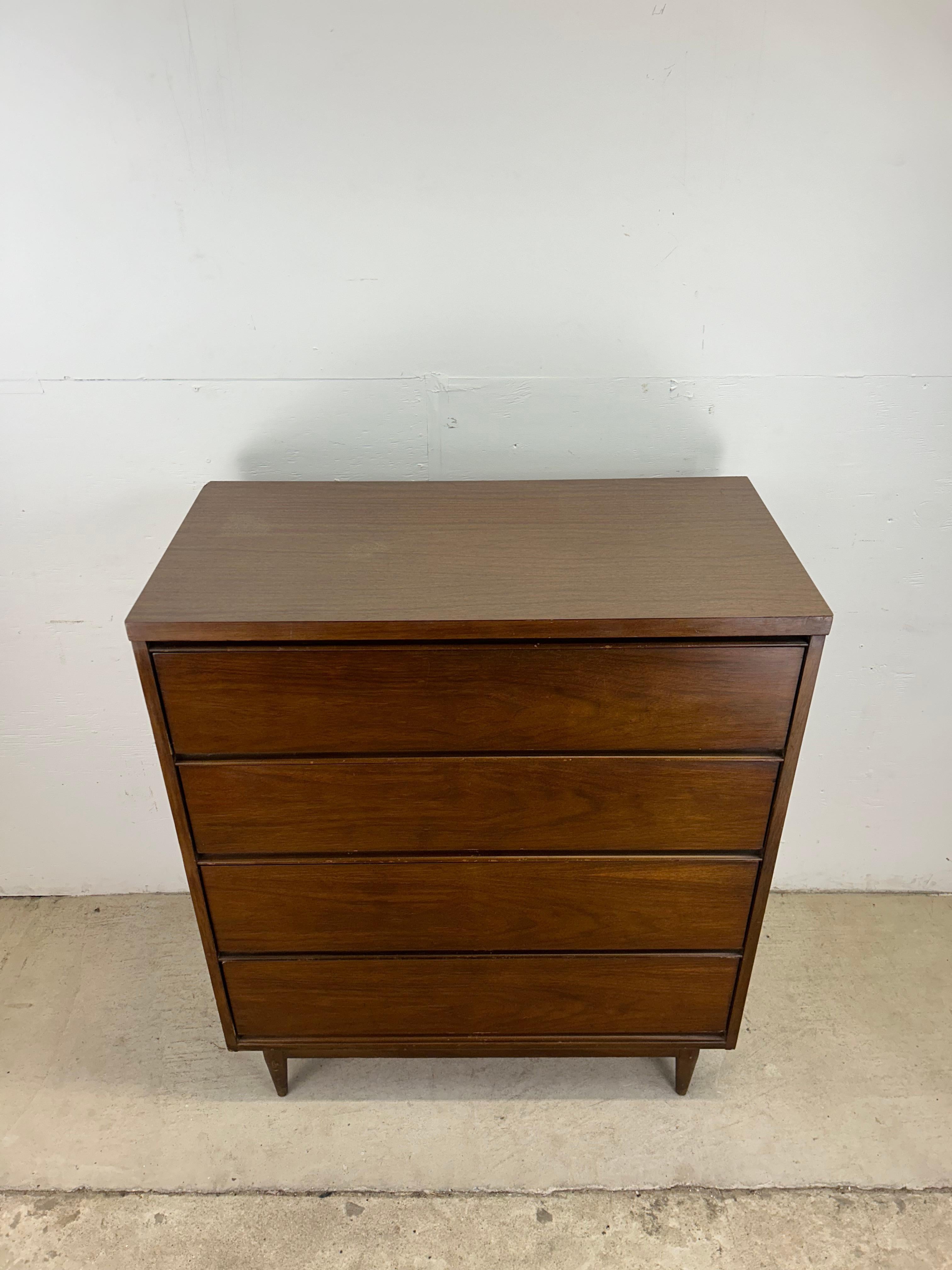This mid century modern highboy dresser features hardwood construction, beautiful walnut veneer with original finish, durable formica top with faux wood grain, four dovetailed drawers with carved wood pulls, and tapered legs. 

Dimensions: 36.25w