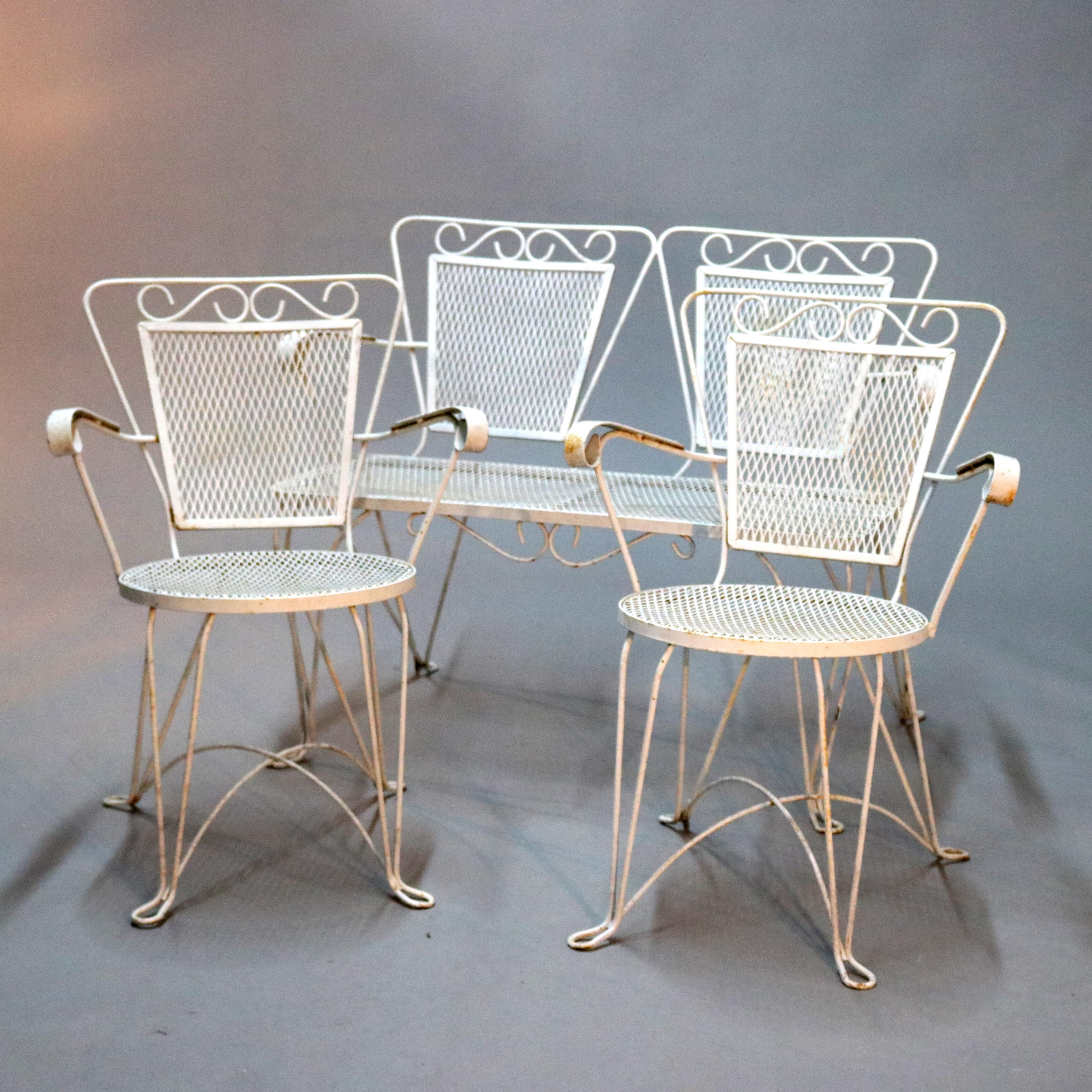 A Mid-Century Modern 4-piece garden patio set offers white painted metal construction having scroll arms, ice cream parlor wire legs with mesh seats and backs, includes a double bench (settee), two armchairs and a side table, circa