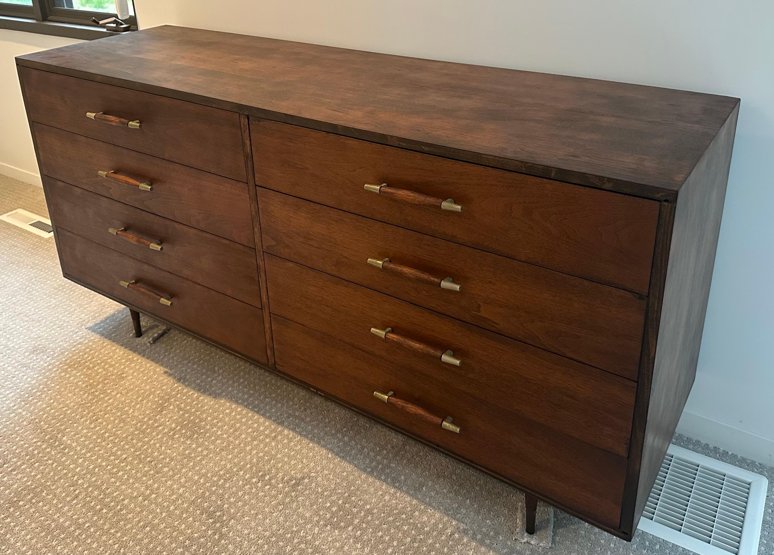 Un comò vintage del Mid-Century realizzato con un legno ricco che mostra le venature naturali e i toni caldi che definiscono lo stile Mid-Century.  Il pezzo comprende sei cassetti spaziosi, sostenuti da gambe e maniglie in ottone che aggiungono