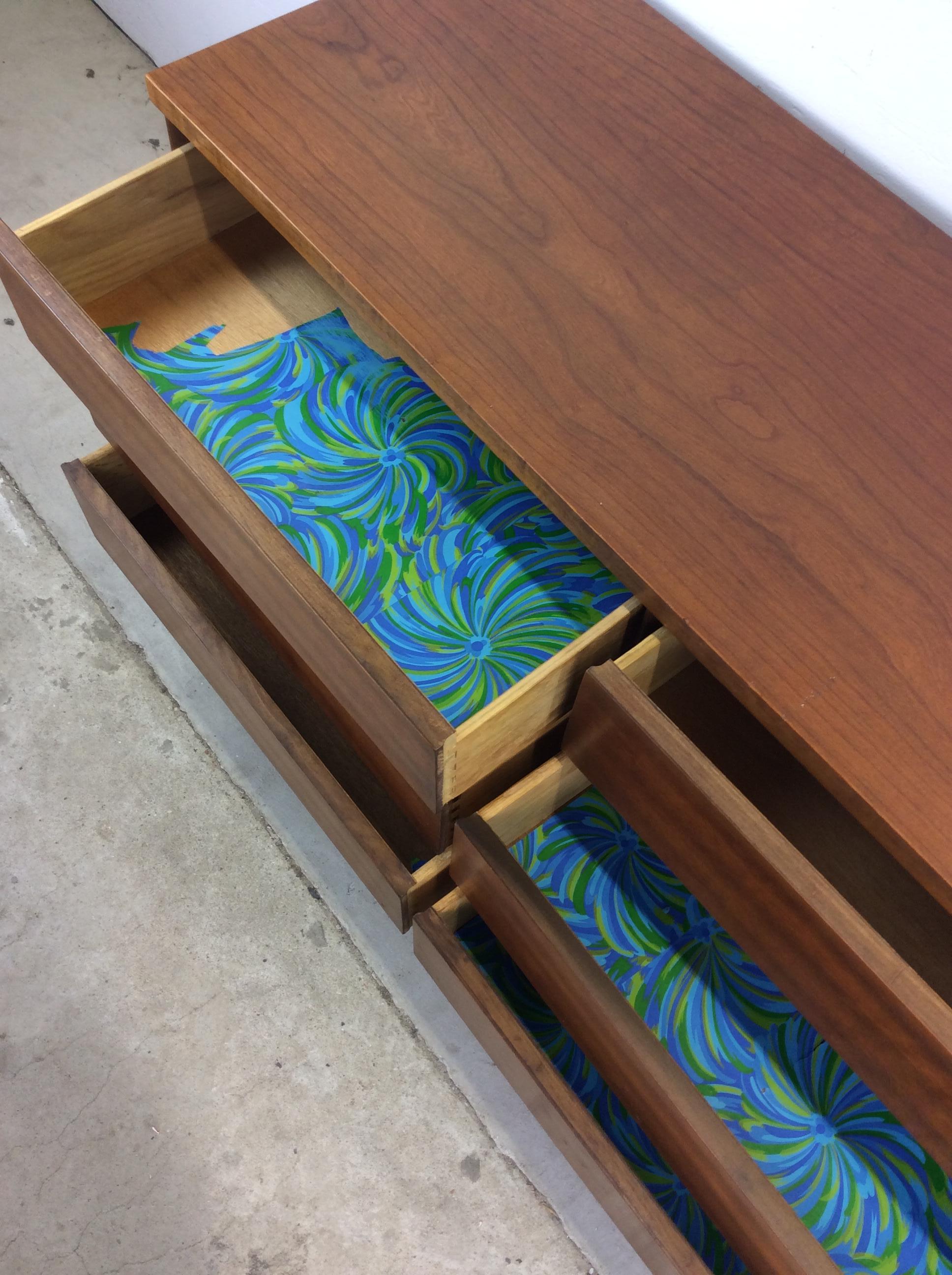 This mid century modern lowboy dresser features hardwood construction, beautiful walnut veneer with original finish, six dovetailed drawers with carved edge drawer pulls, wood top, and tall tapered legs.

Dimensions: 52w 17.75d 30.5h

Condition