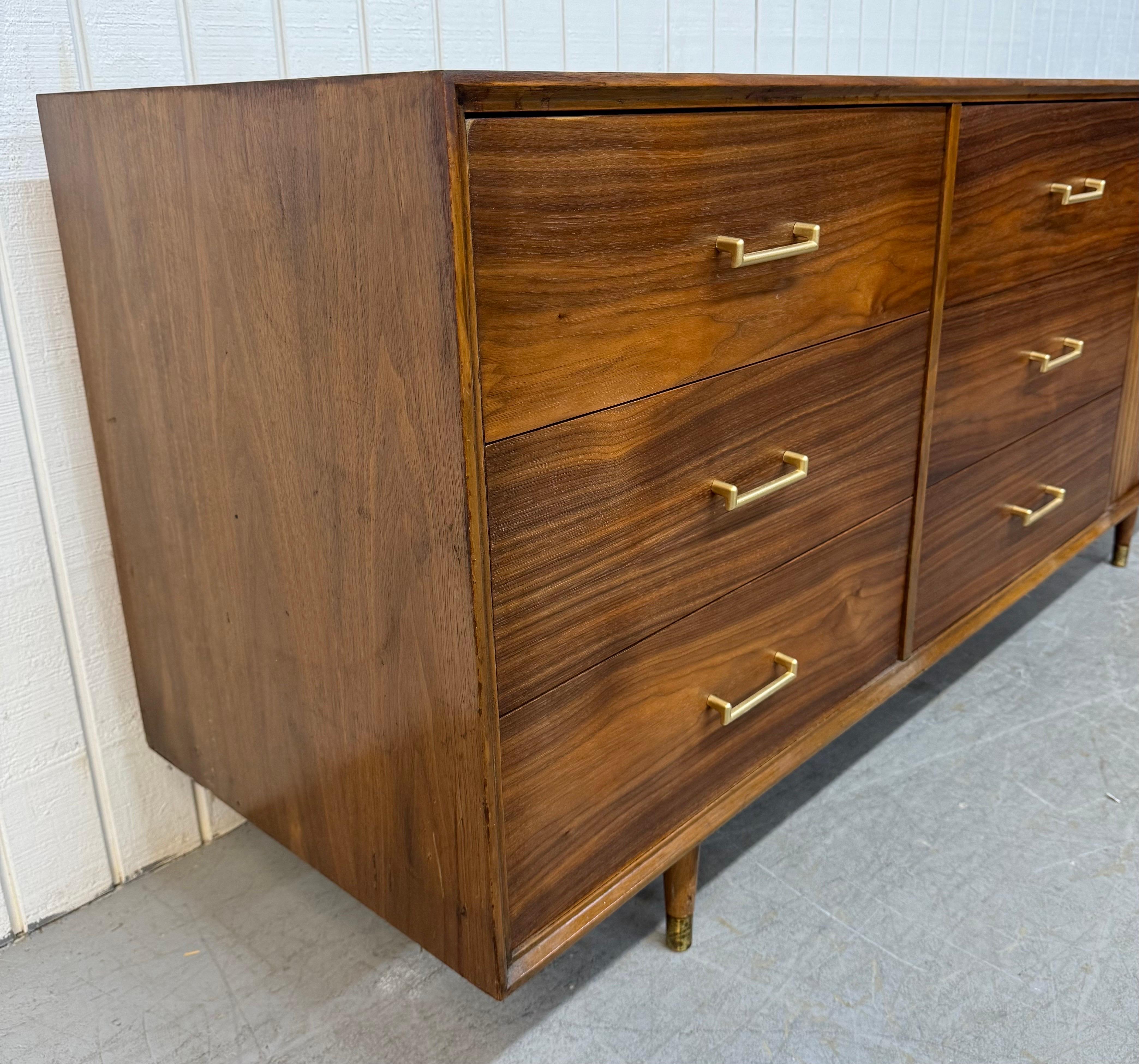 Questo annuncio si riferisce a un comò a 9 cassetti in legno di noce di epoca moderna. Caratterizzato da un design lineare, sei ampi cassetti sul lato sinistro con tiretti originali in ottone, un'anta a tamburo sul lato destro che si apre su tre
