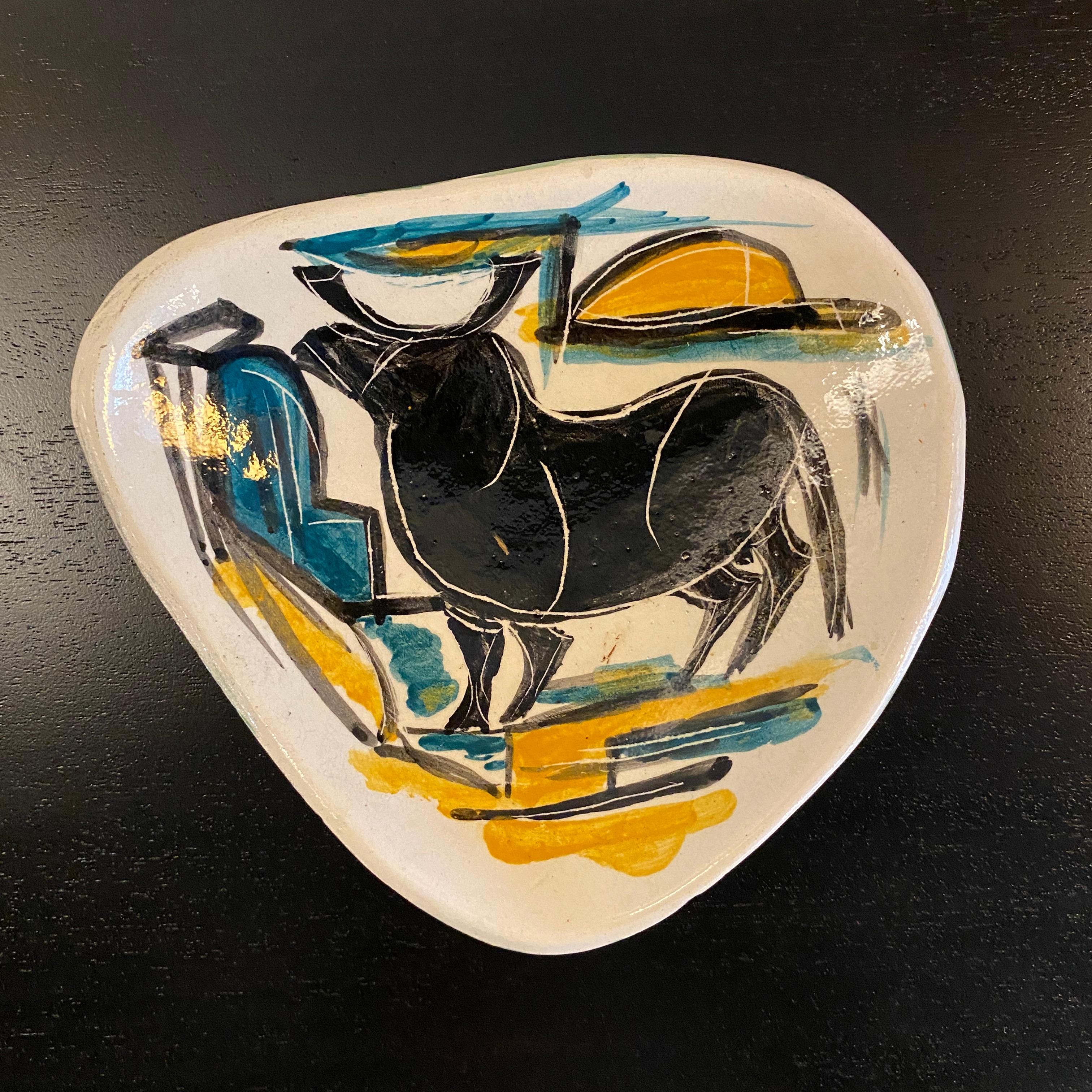 Mid century modern, hand-painted, art pottery dish features an abstract bull scene in bold black, teal and yellow brush strokes against a white background. The back of the piece is a dark teal green. The dish is an irregular triangular shape with a