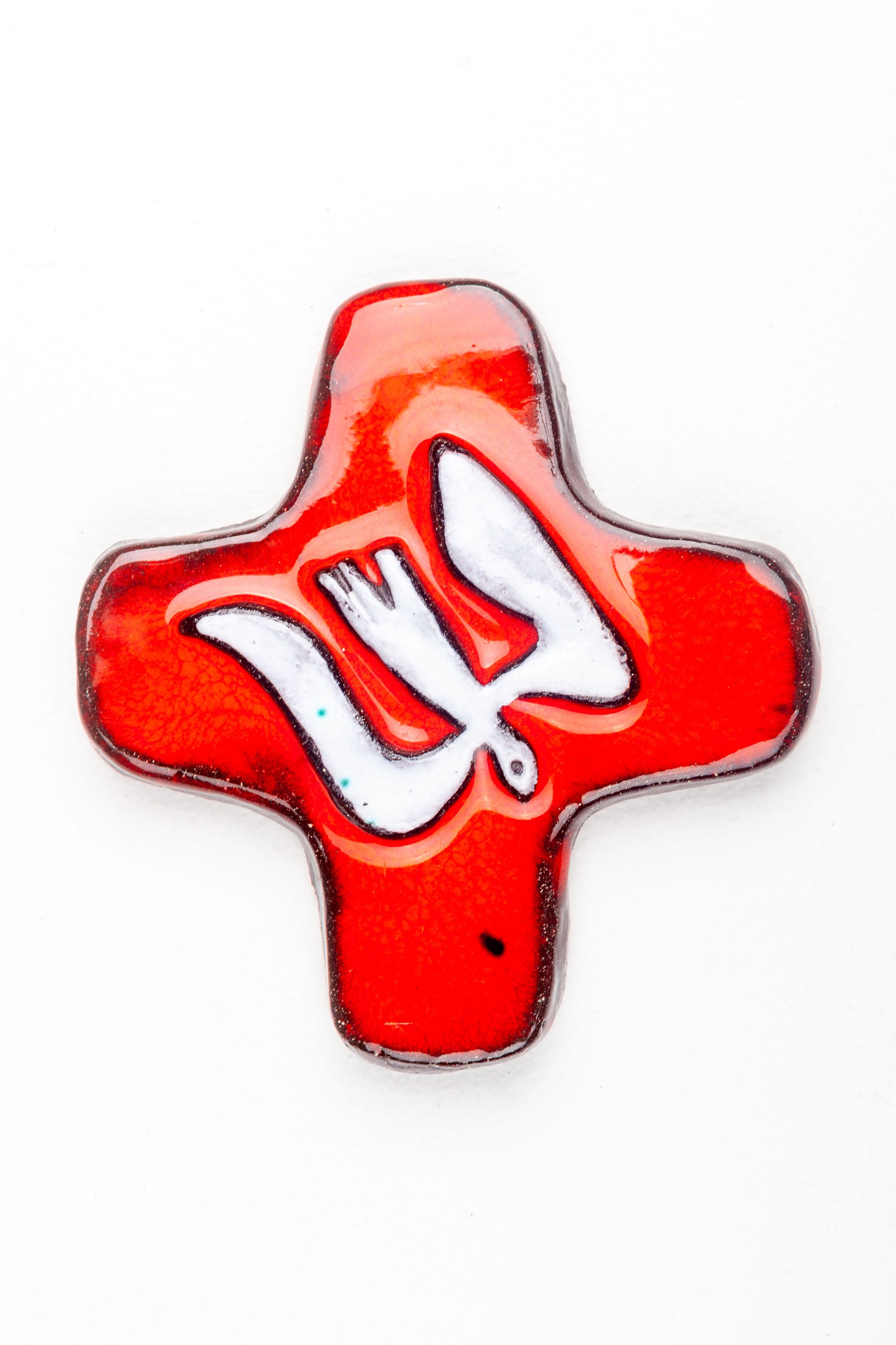 This mid-century modern ceramic cross showcases the bold, expressive aesthetic that was prevalent among European studio pottery artists during the 1950s to 1970s. The vivid red glaze serves as a dramatic backdrop to the abstract white dove form at