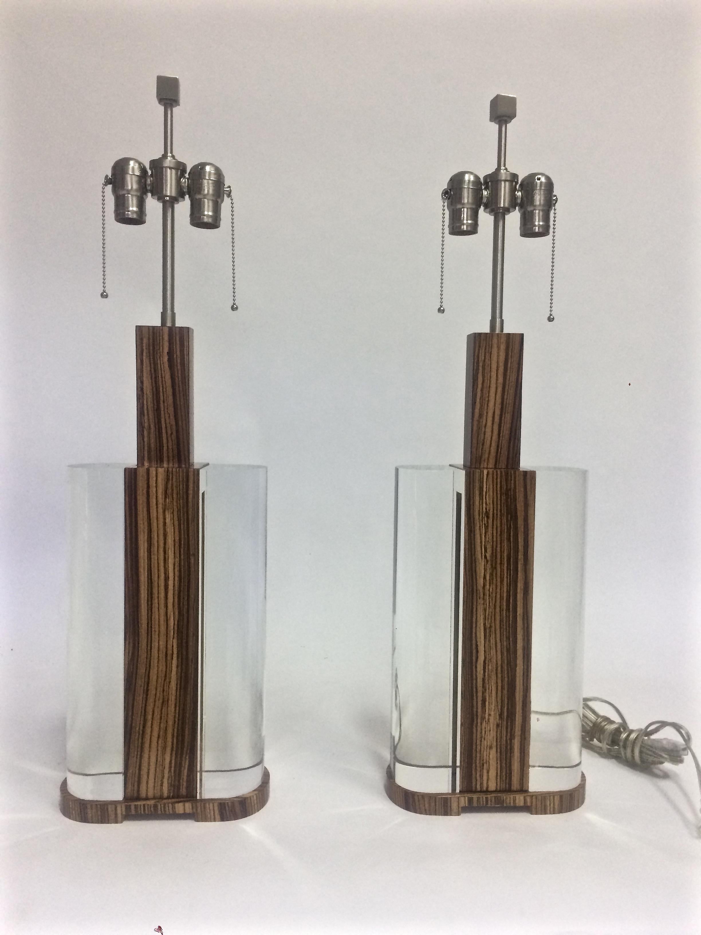 Mid-Century Modern acrylic and zebra wood pair of lamps, the solid satin stainless steel dual light sockets with a square finial to lock the shade and an on/off pull chain over a supporting zebra wood standard, the body is comprised of a massive