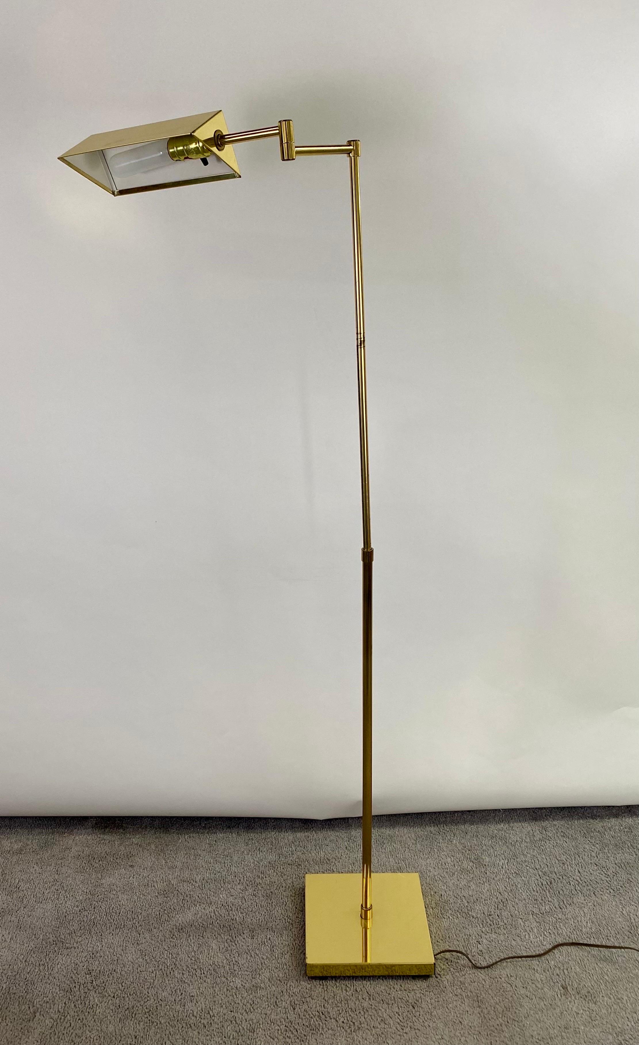  A classy Mid-Century Modern pharmacy floor lamp made of brass. The lamp features an adjustable column supported by a square brass base. The shade has a tented shape and swivels from one side to the other.  The mid-century modern pharmacy floor lamp