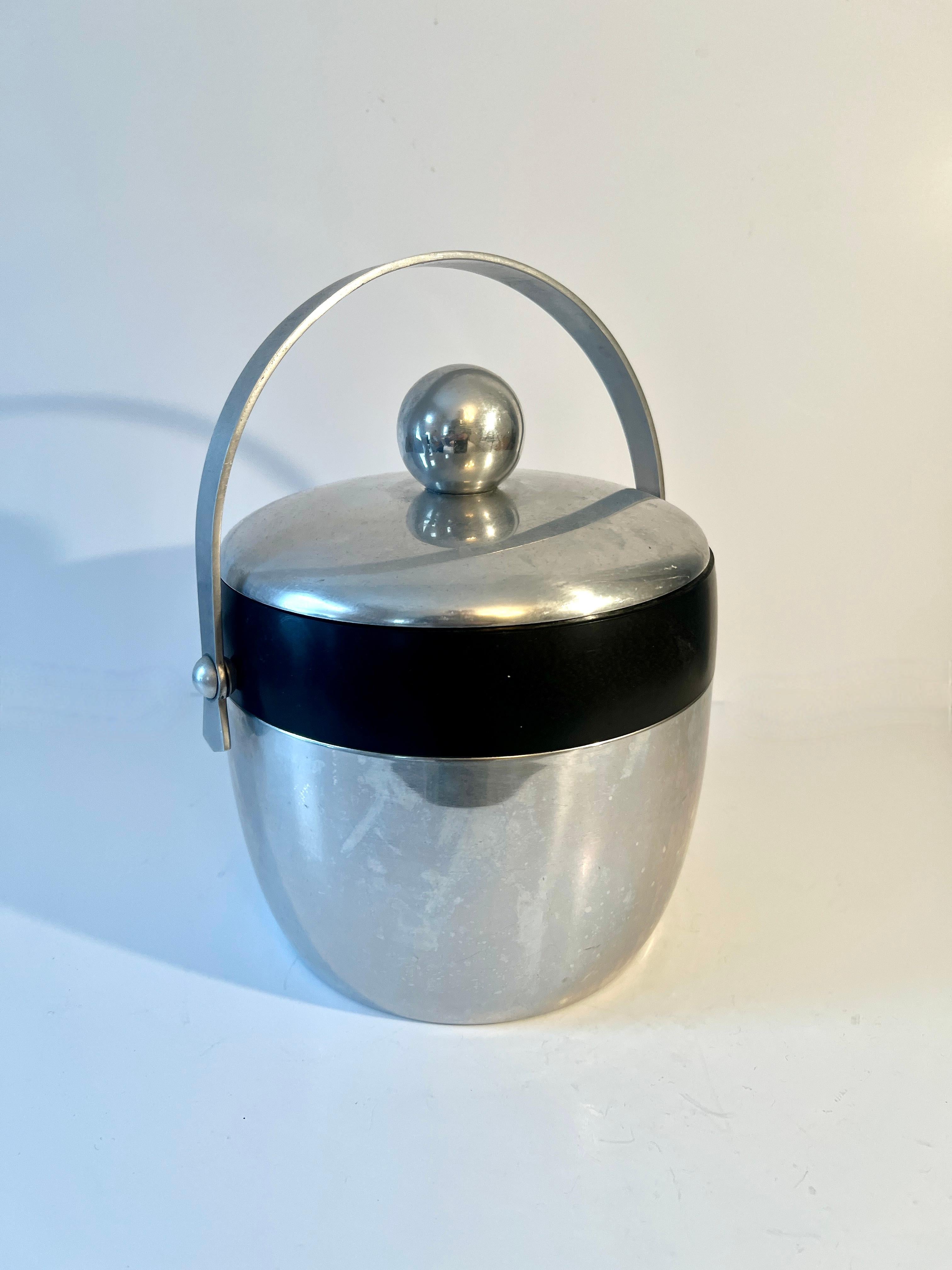 A wonderful, iconic mid-century aluminum ice bucket that will be a star on any bar.  The piece is made of aluminum with a resin or bakelite (?) band around the perimeter. 

A compliment to any space, on the bar, used outdoors for entertaining or