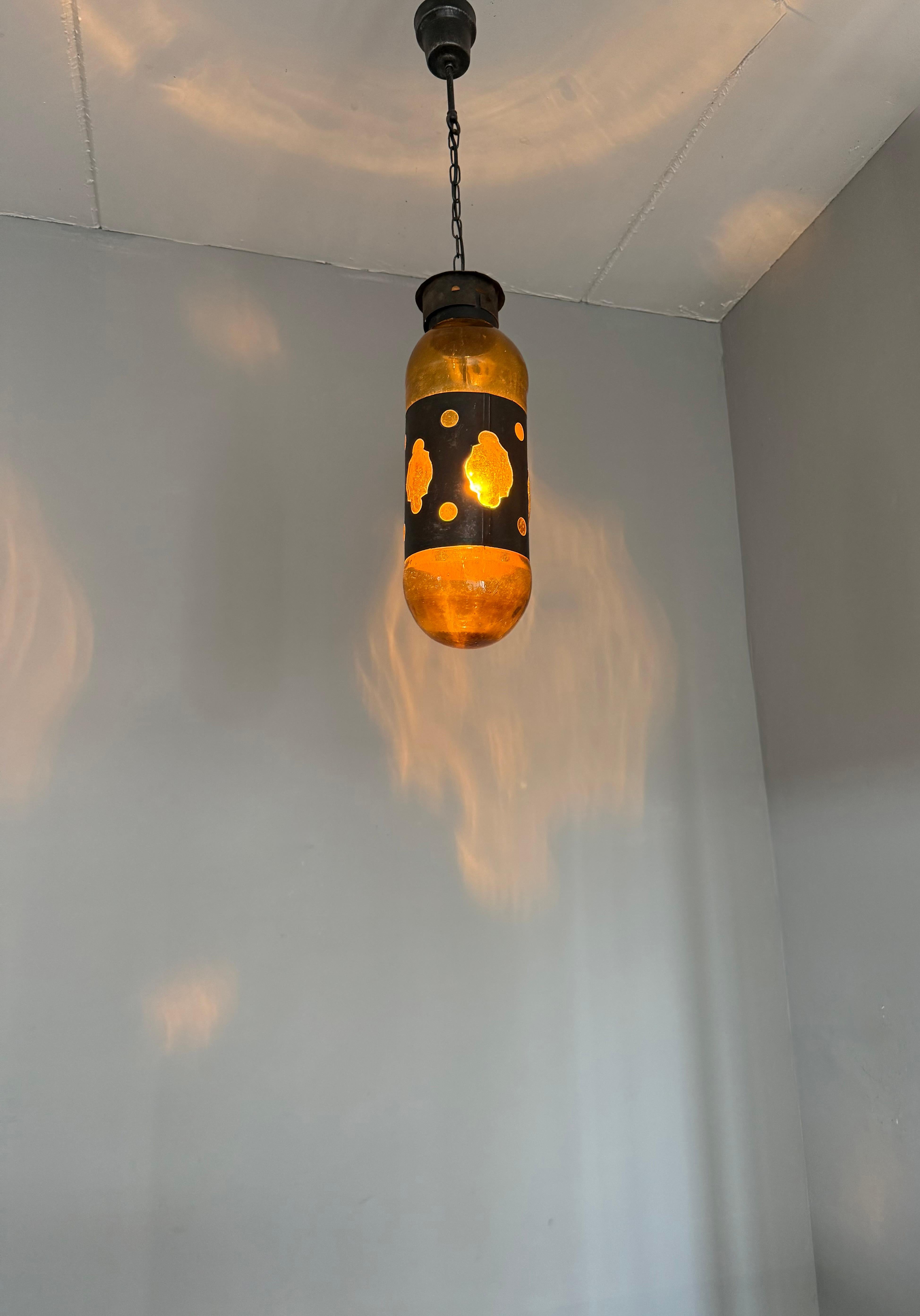 Beautiful color and large size fixture with mouth blown glass in a capsule/cylinder shape frame.

A rare and striking pendant lamp featuring thick amber hand-blown glass encased in a patinated metal sheath, reminiscent of the Brutalist aesthetic.