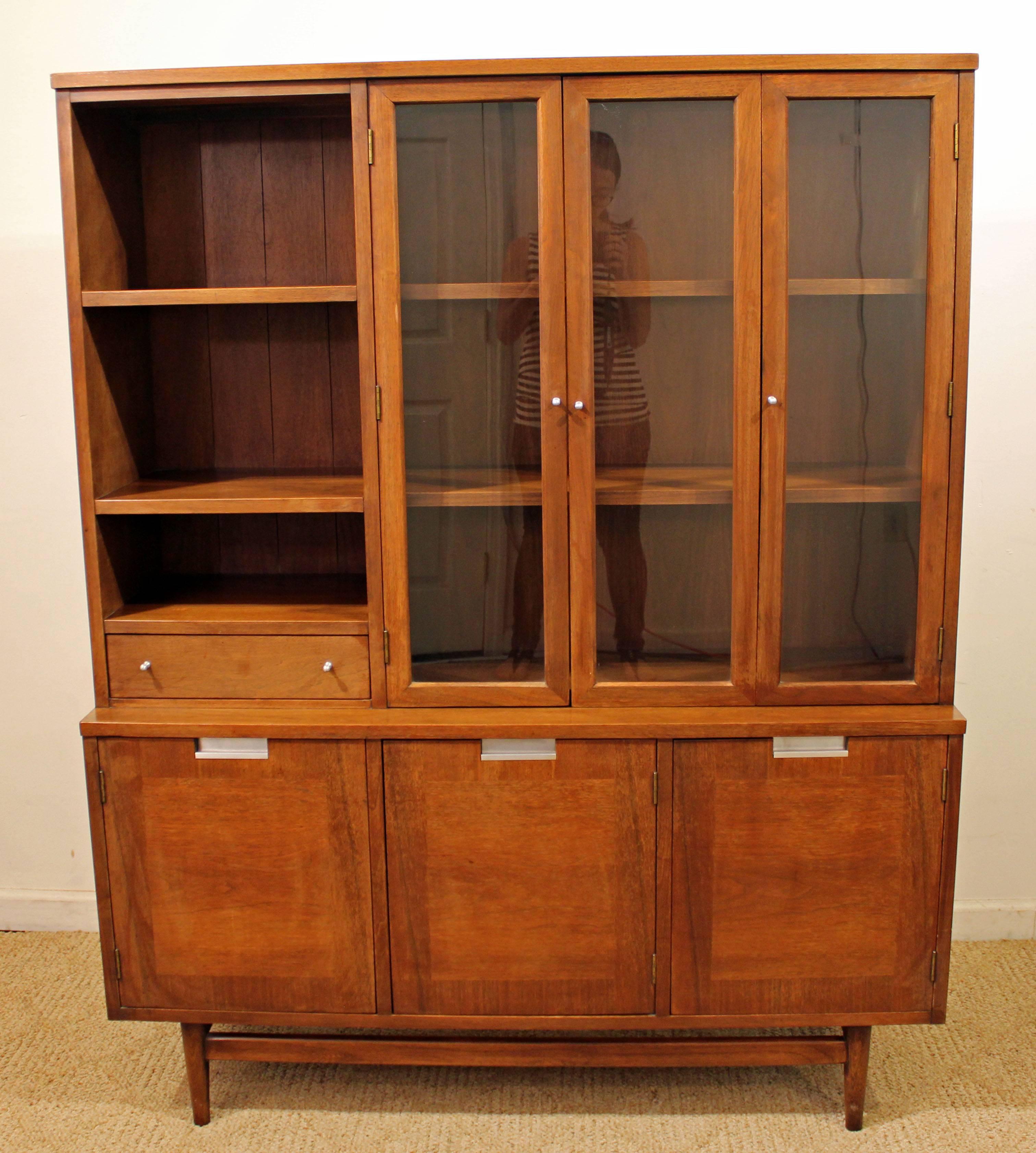 This is a walnut china cabinet with two glass doors and shelving on top and three cabinets underneath. Features brushed aluminium pulls. It was made by American of Martinsville.