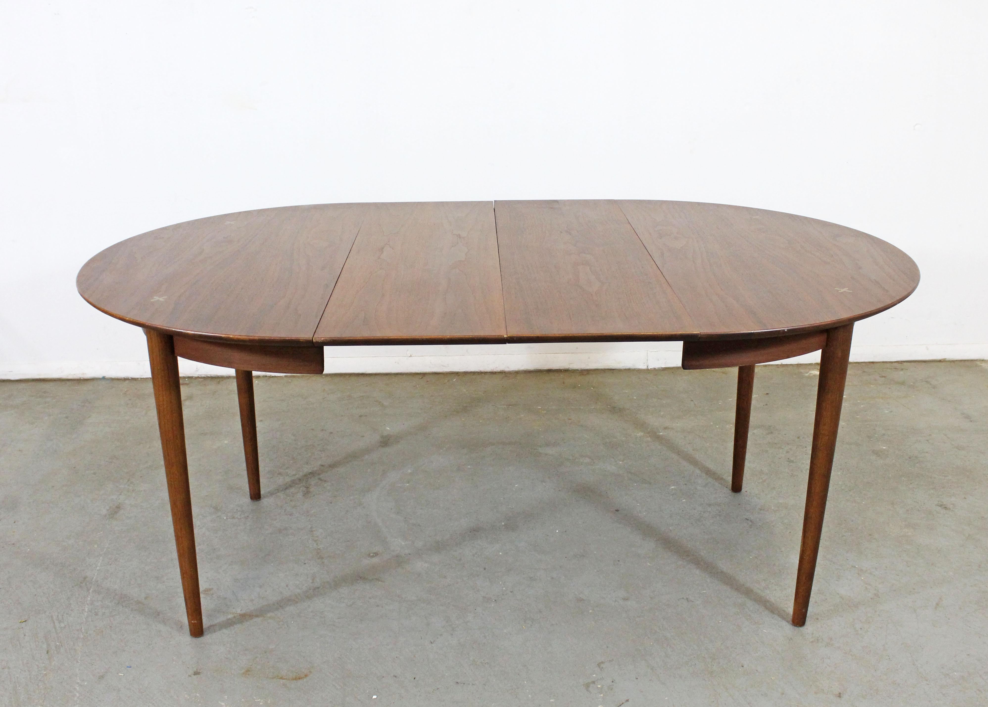 Offered is a vintage Mid-Century Modern walnut dining table made by American of Martinsville. This table features a rounded top and inlaid metal x's; an iconic feature in many pieces by American of Martinsville. Includes two extension boards, which